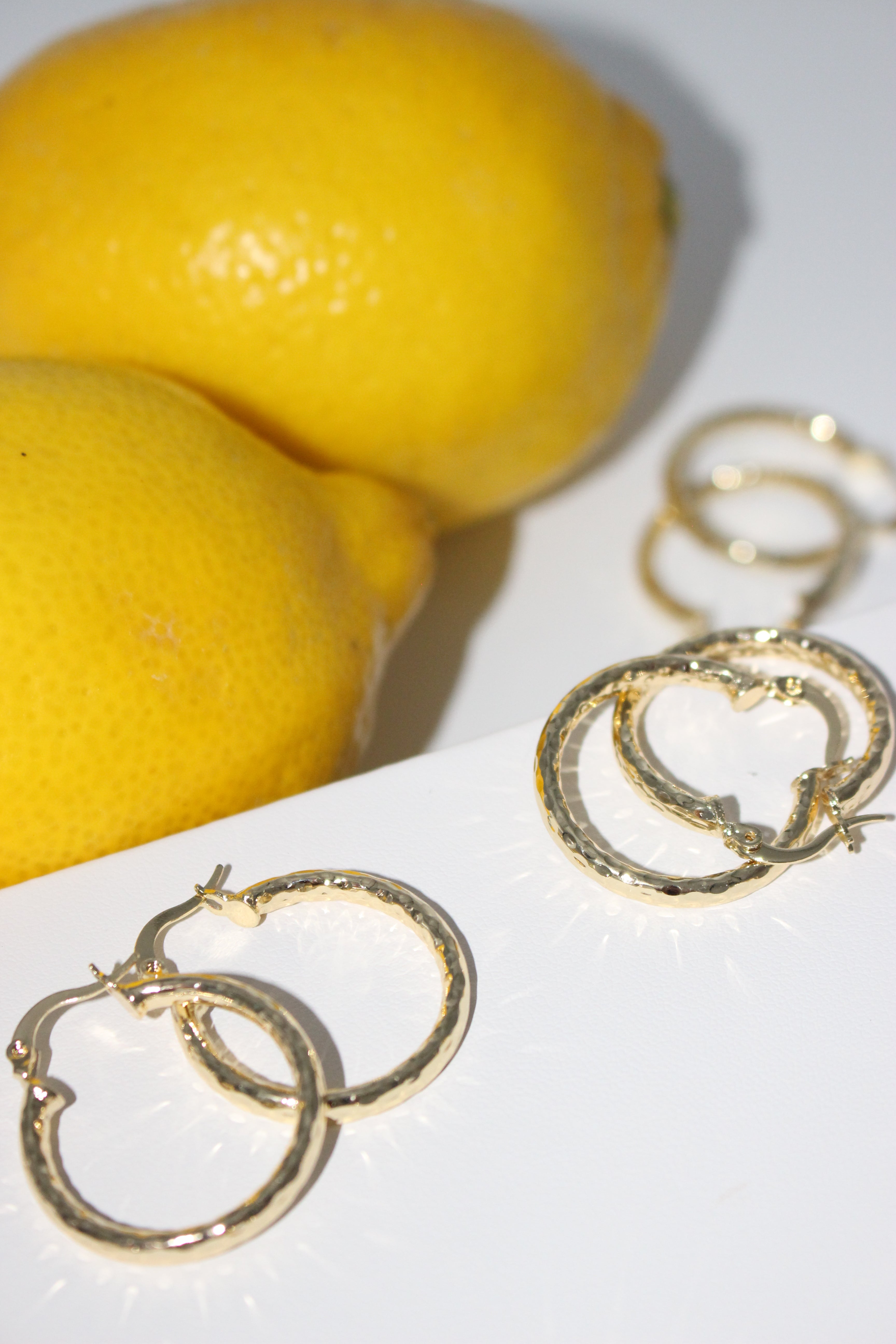 Gold hoop earrings next to two lemons on a white background