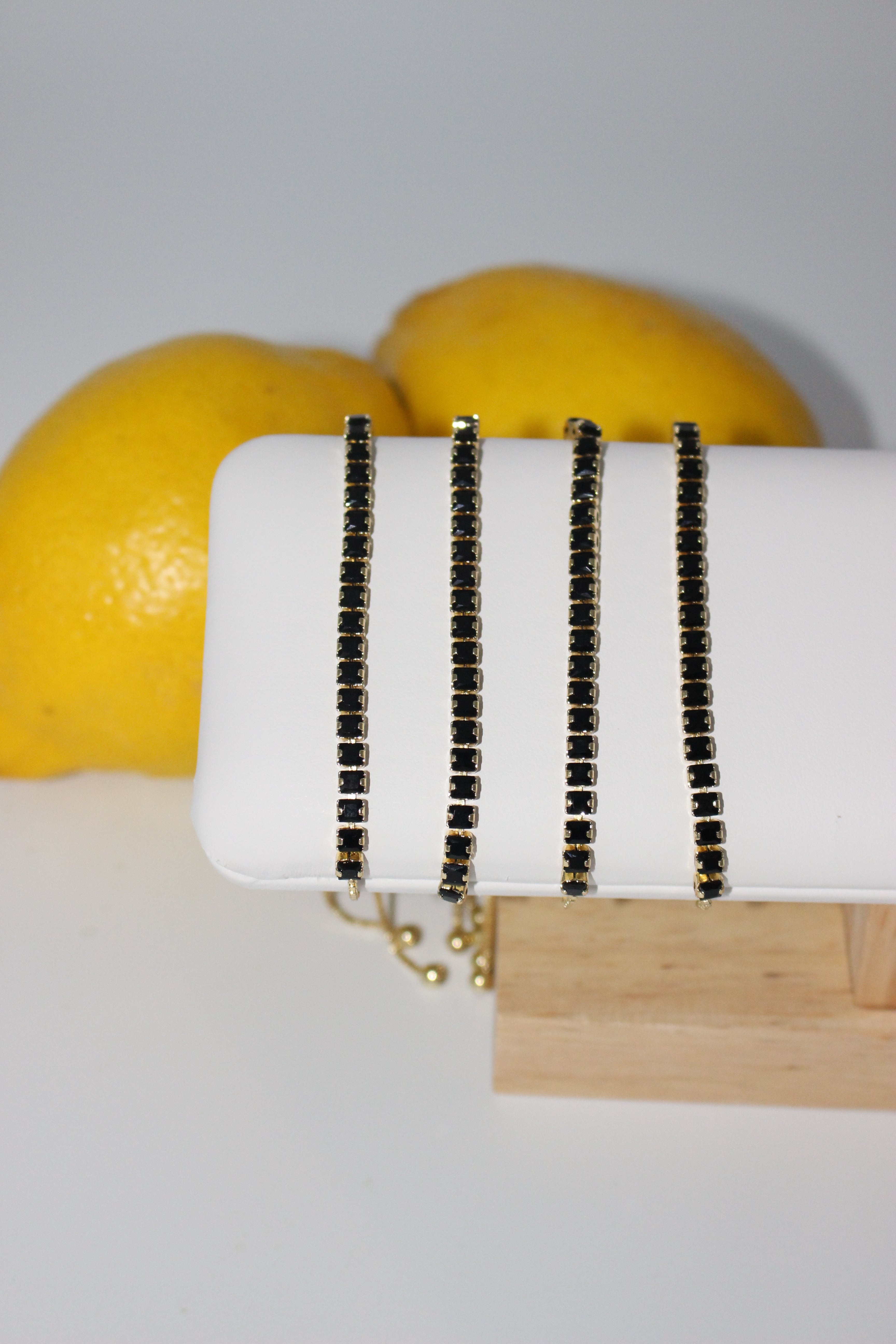 Gold bracelet with black gemstones on a wooden stand with lemons in the background