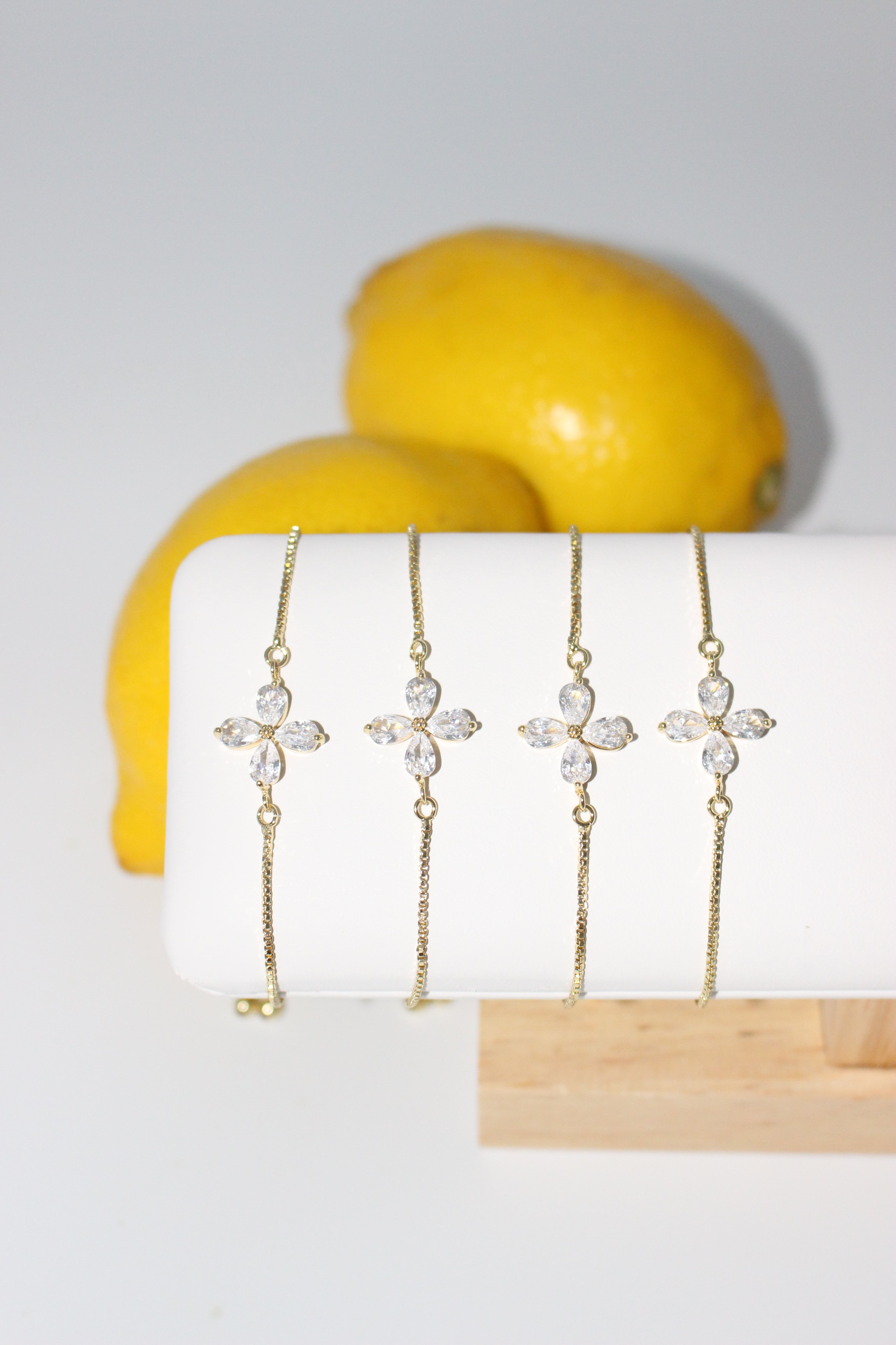 Set of gold bracelets with crystal accents on a white surface with yellow fruits in the background