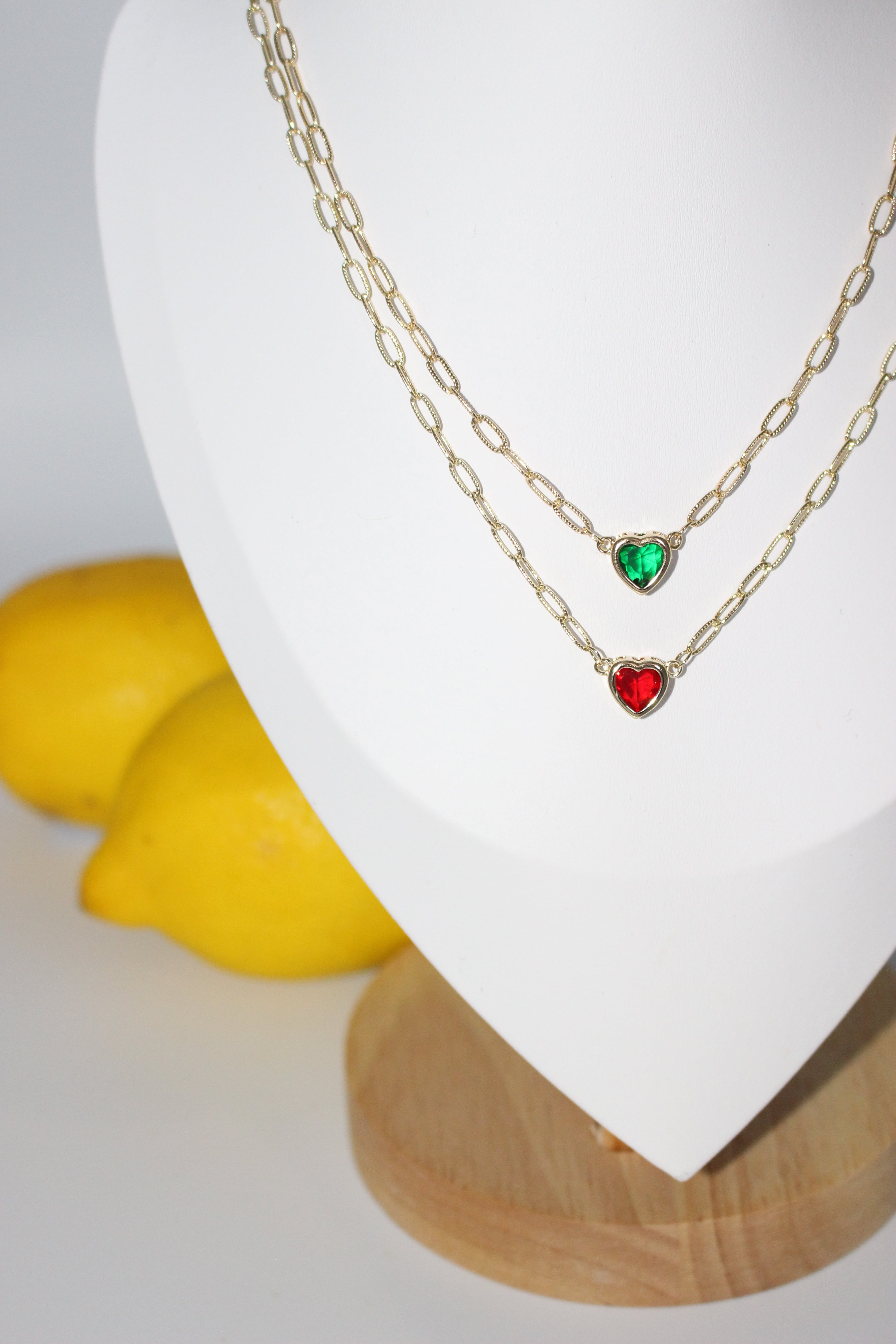 Gold chain necklace with red and green gemstones on a white surface.