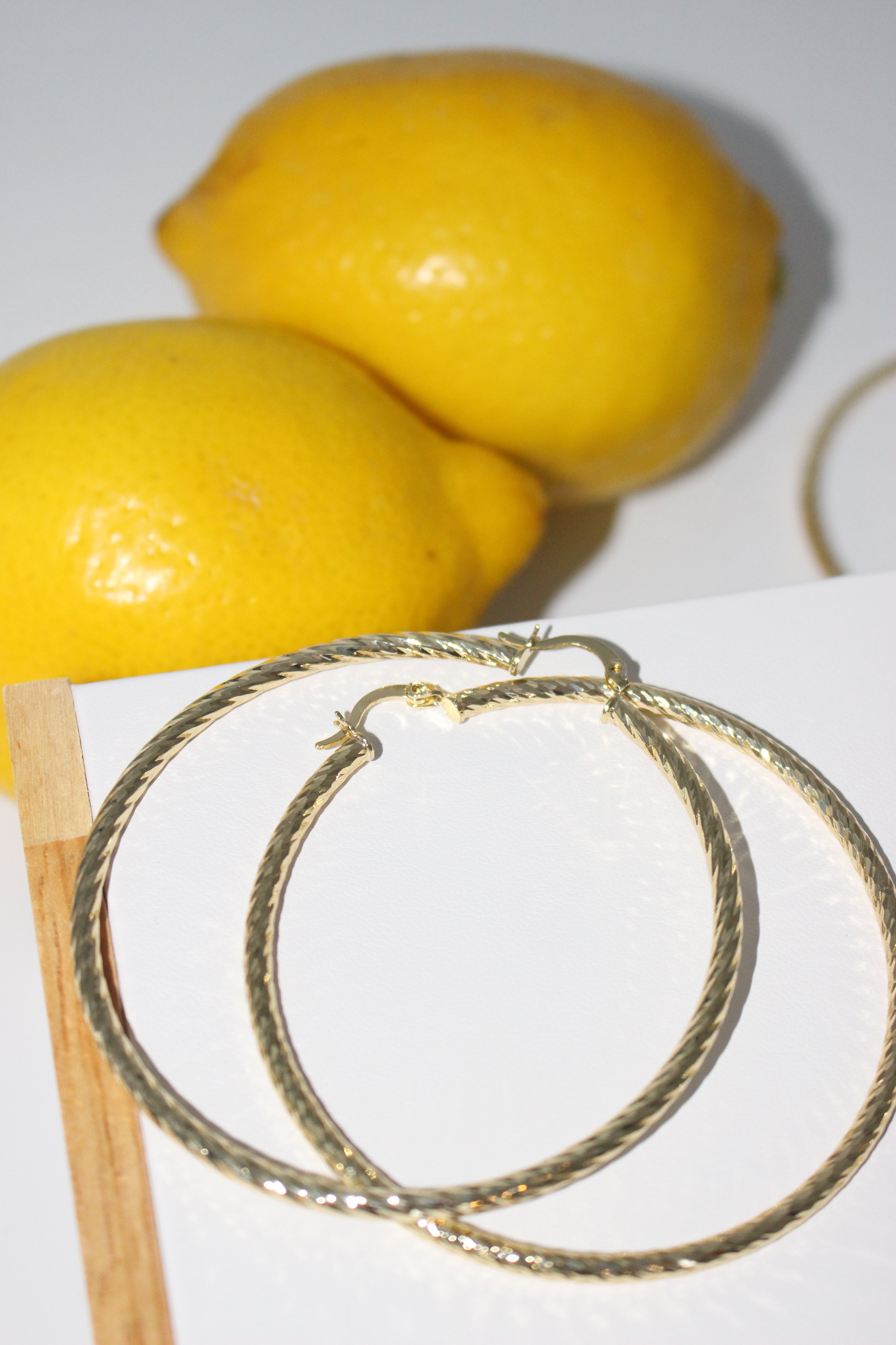 Gold hoop earrings next to two lemons on a white background