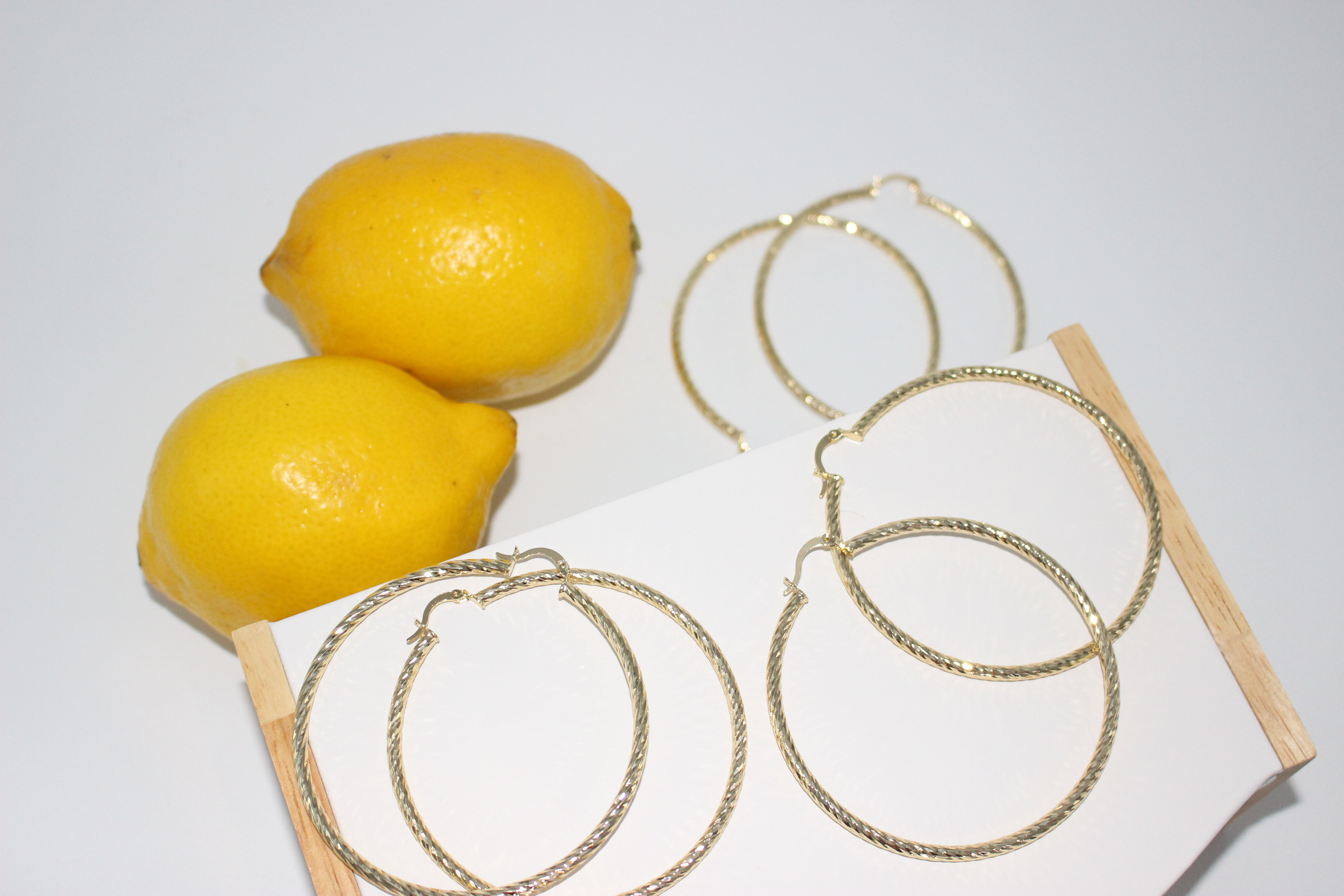 Gold hoop earrings displayed on a white surface with lemons.