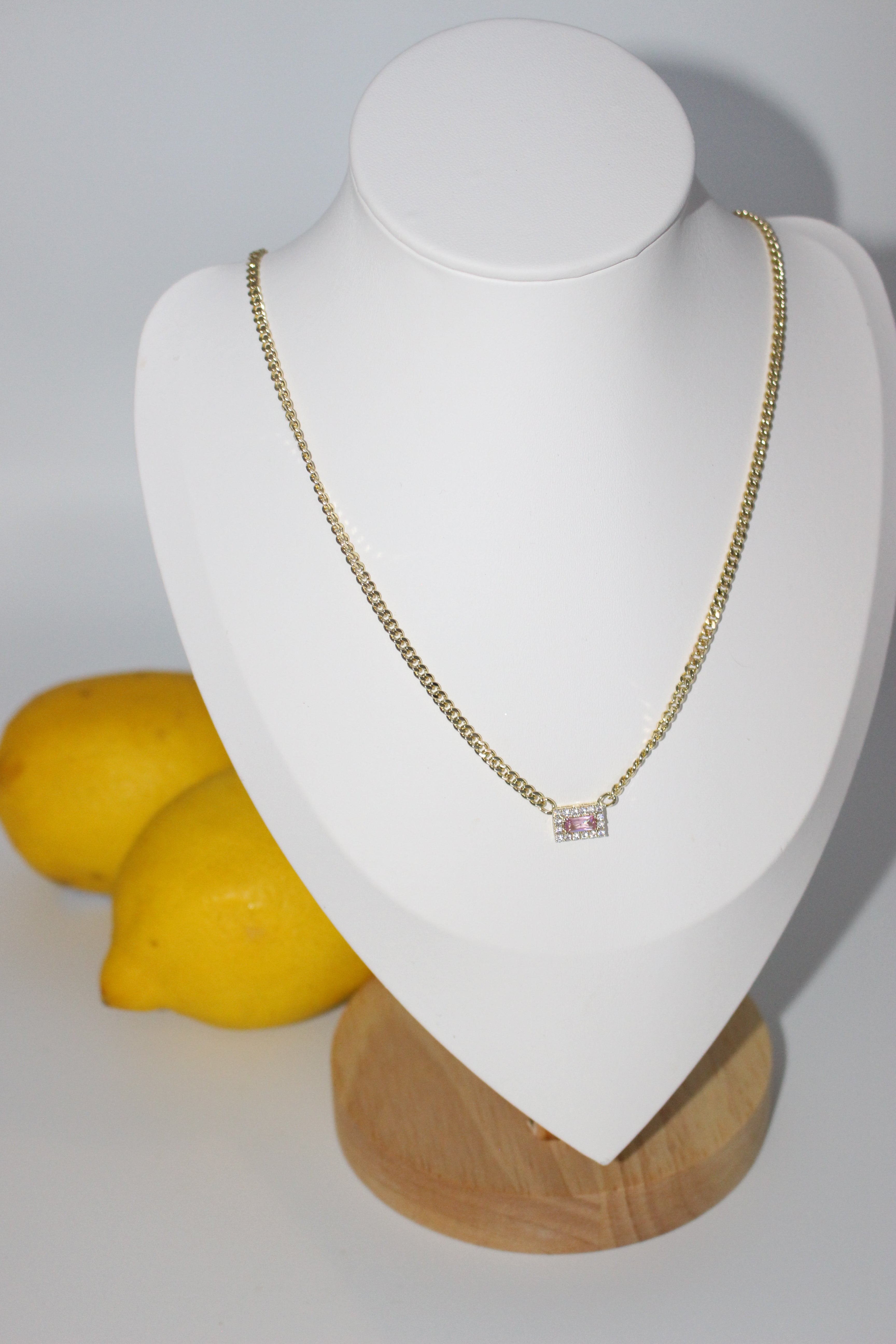 Gold necklace on white surface with lemons in the background