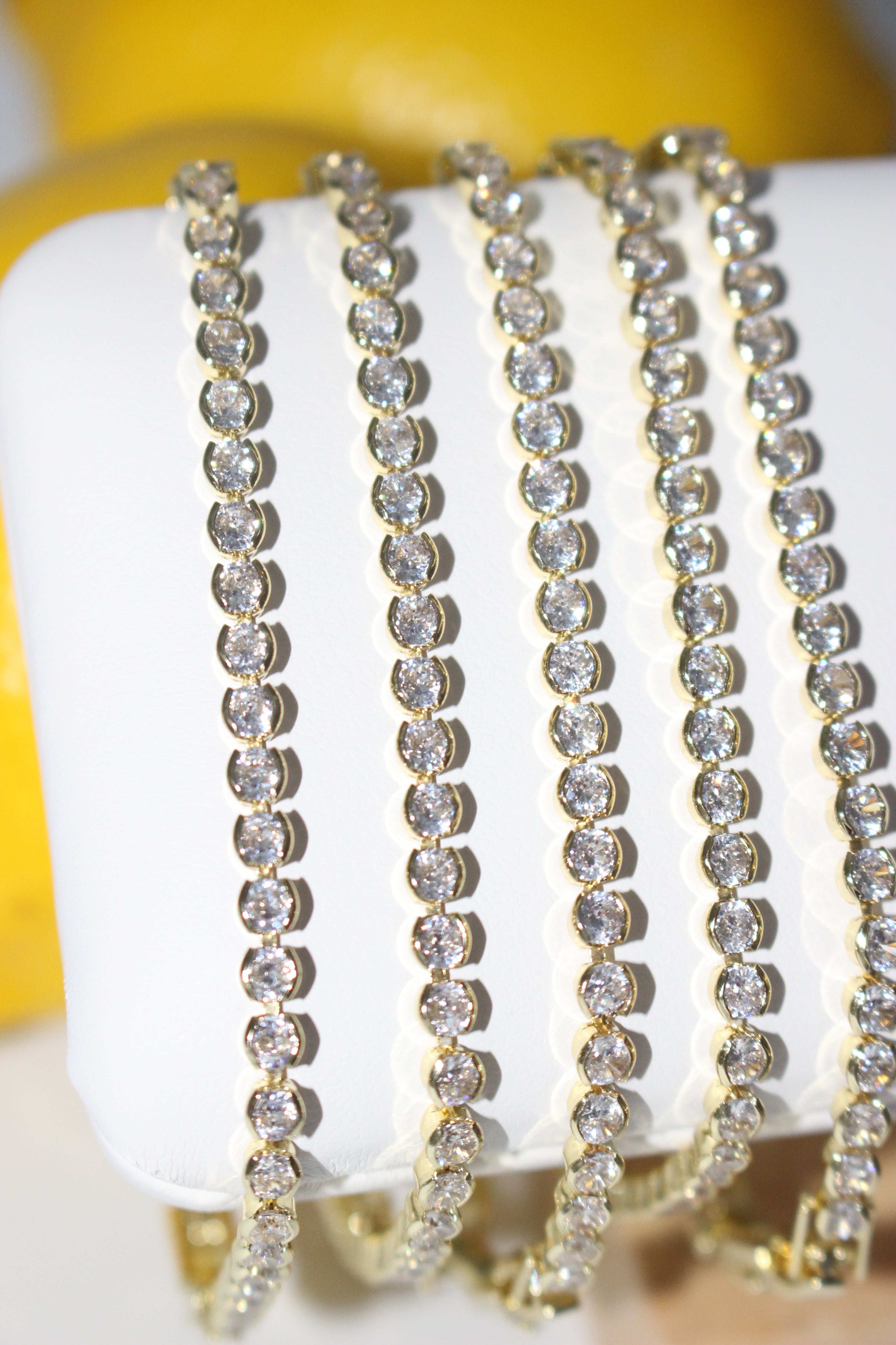 Stack of gold and diamond bracelets on a white mannequin arm with a yellow background