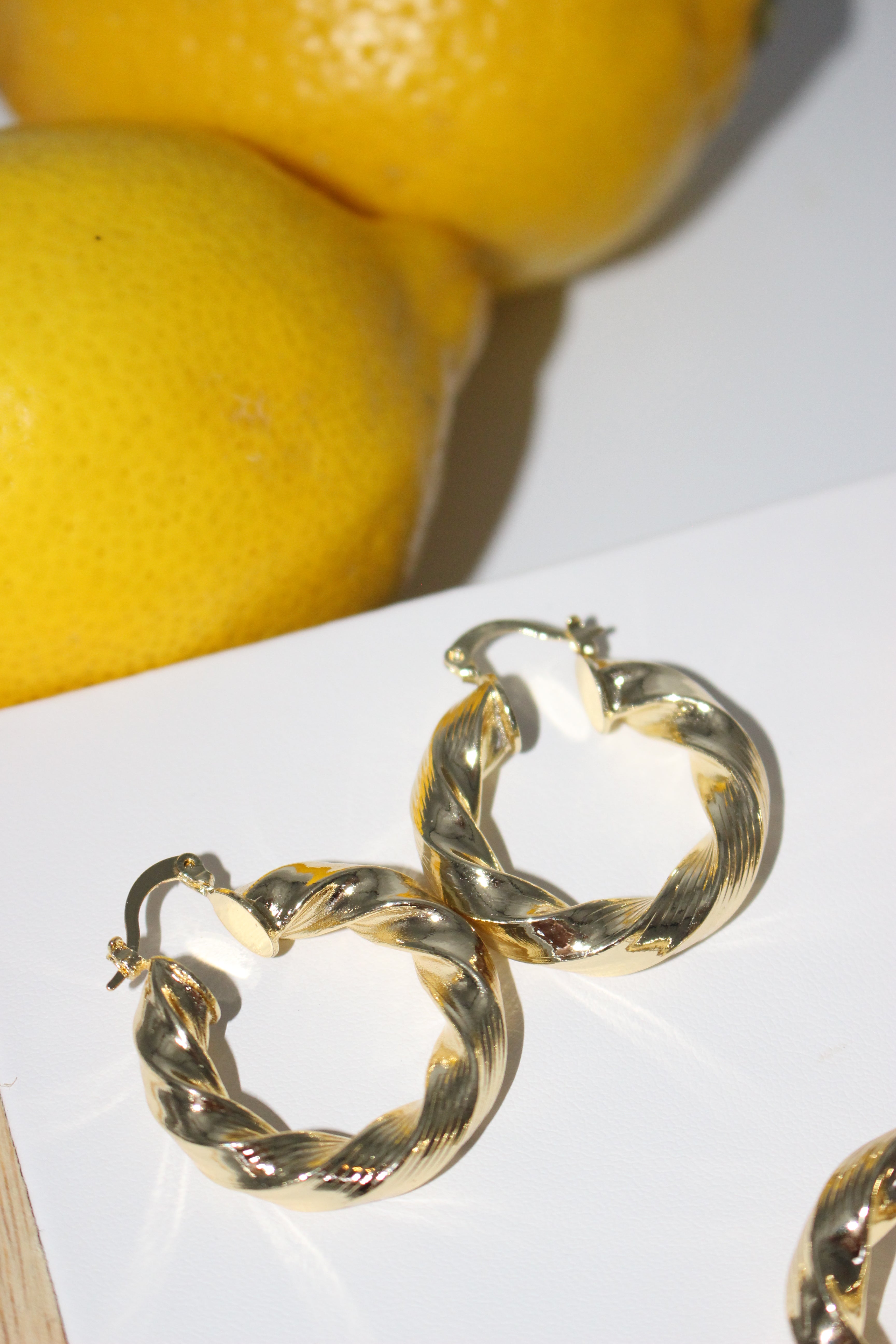 Gold hoop earrings on a white surface with lemons in the background