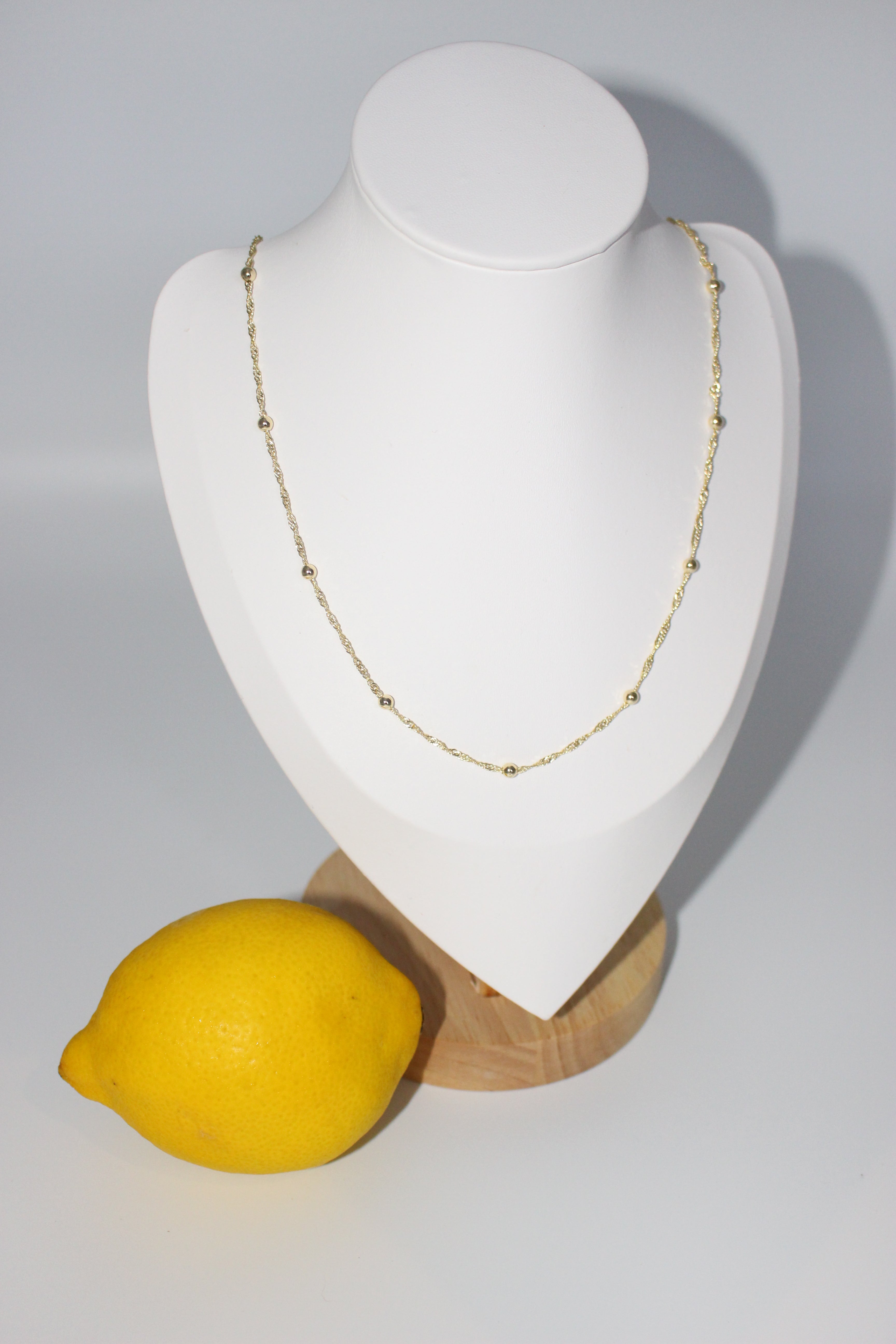 Necklace on white stand next to a lemon.