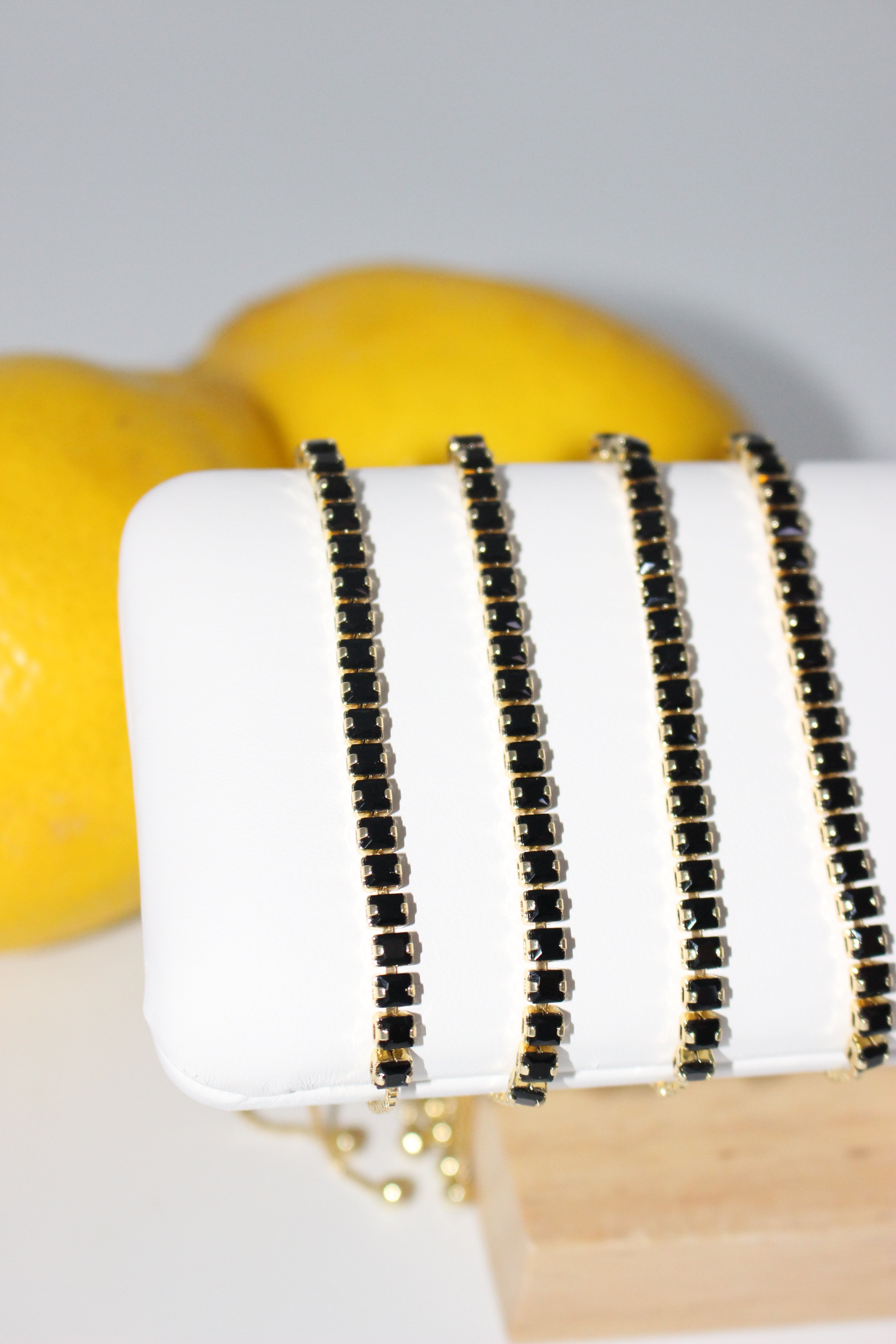 Black beaded bracelet on a white surface with a yellow object in the background