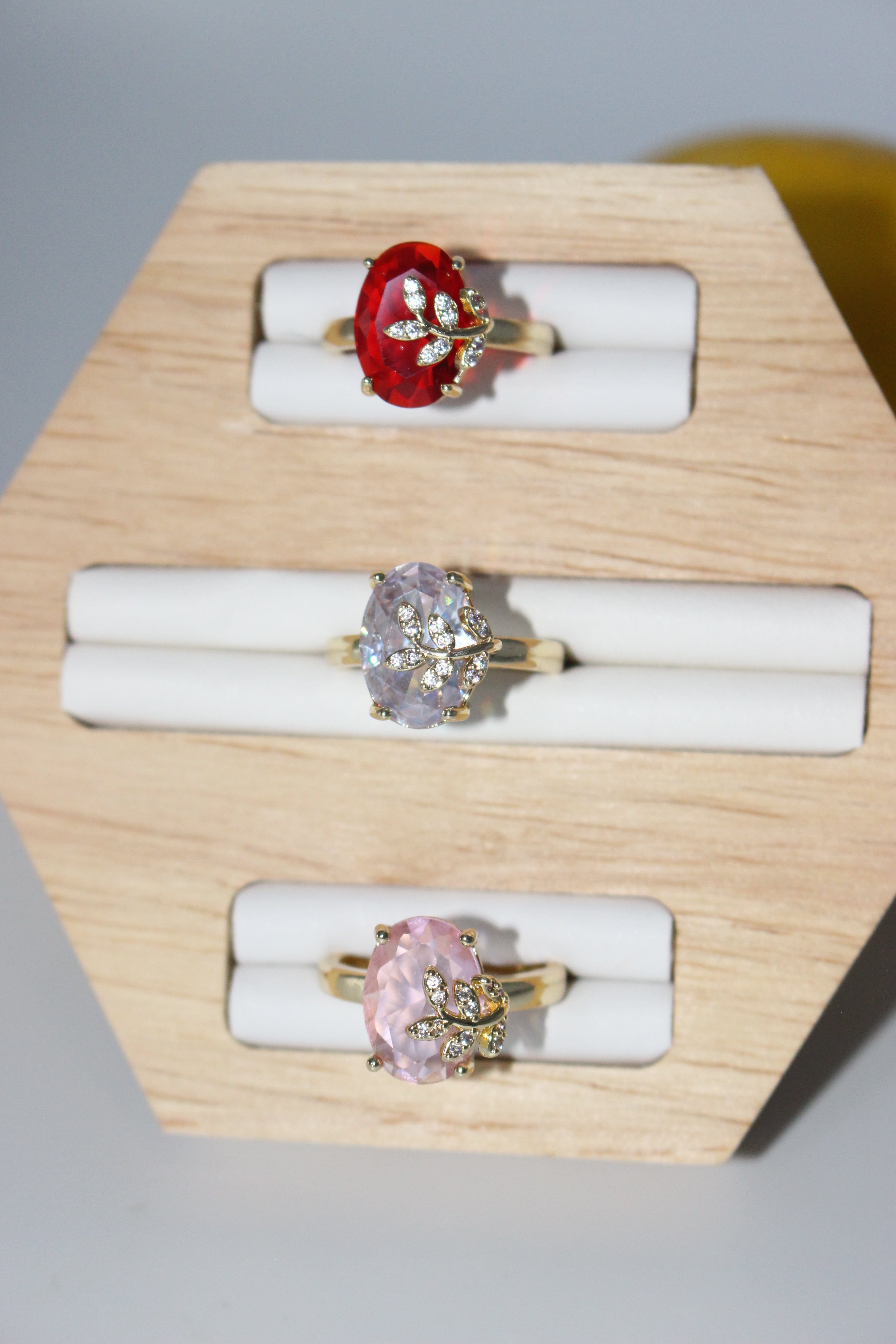 Three rings with different gemstones on a wooden display stand.