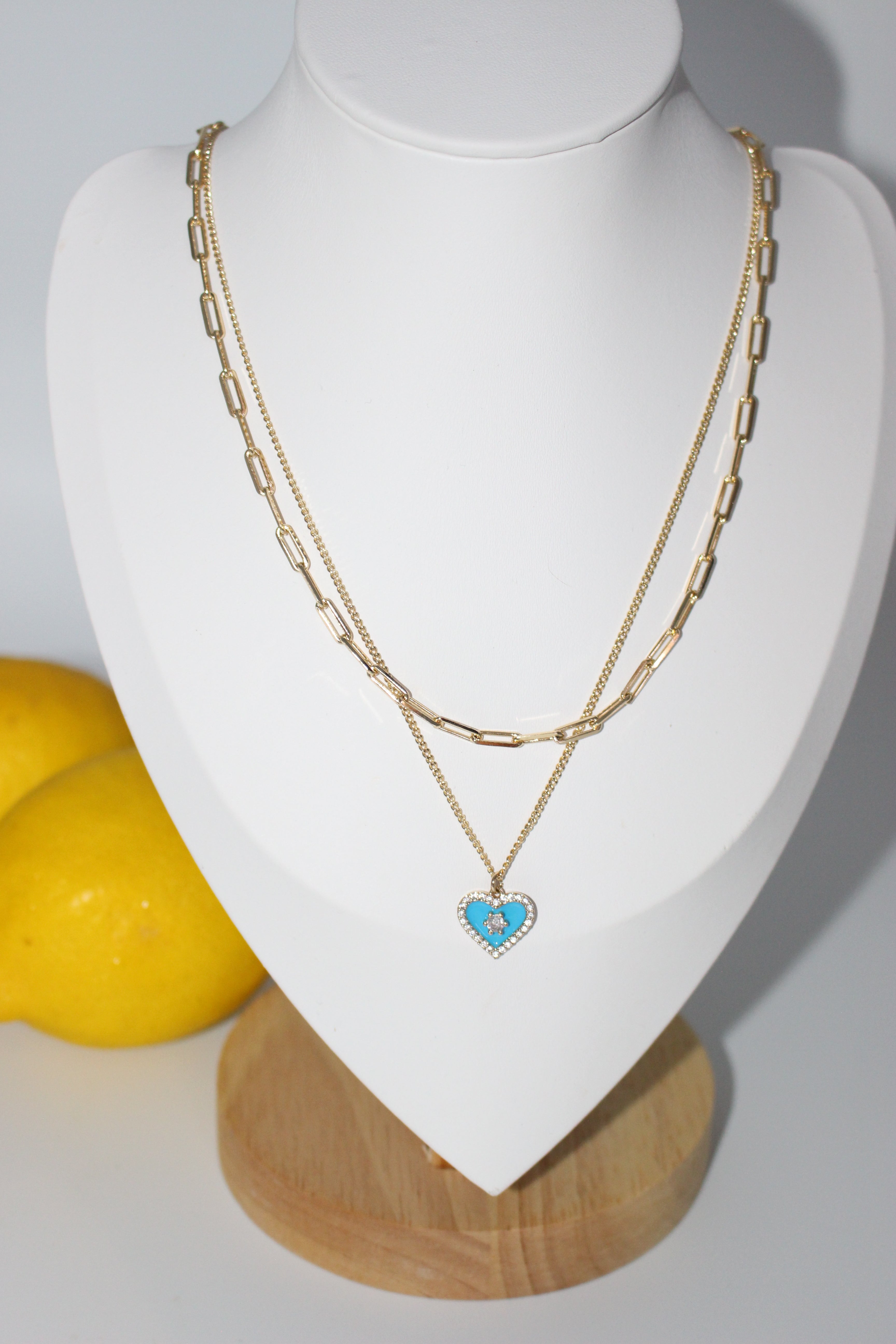 Blue heart & gold necklace on a white stand with lemons in the background