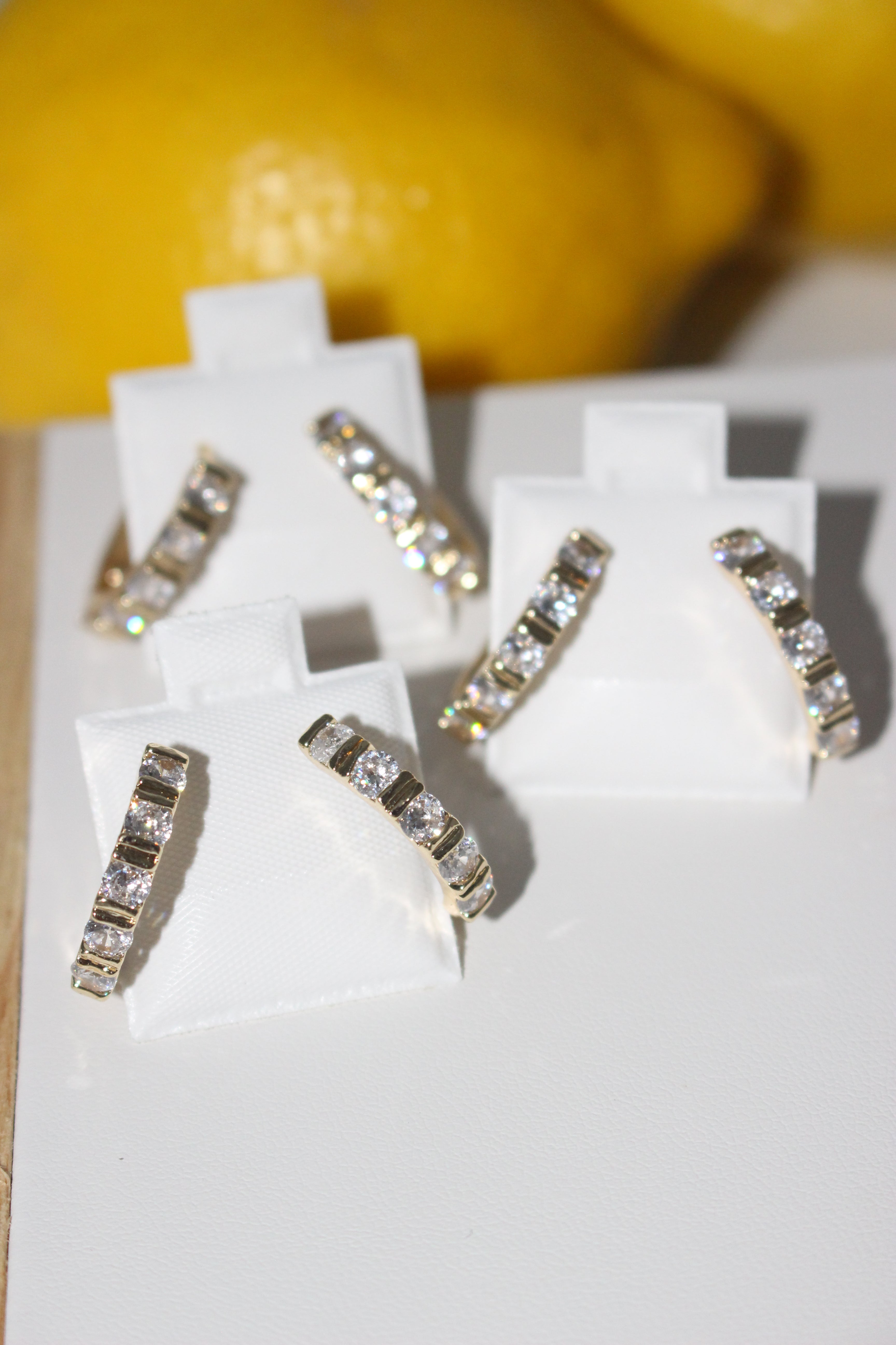 Gold earrings with clear stones on a white stand against a blurred background