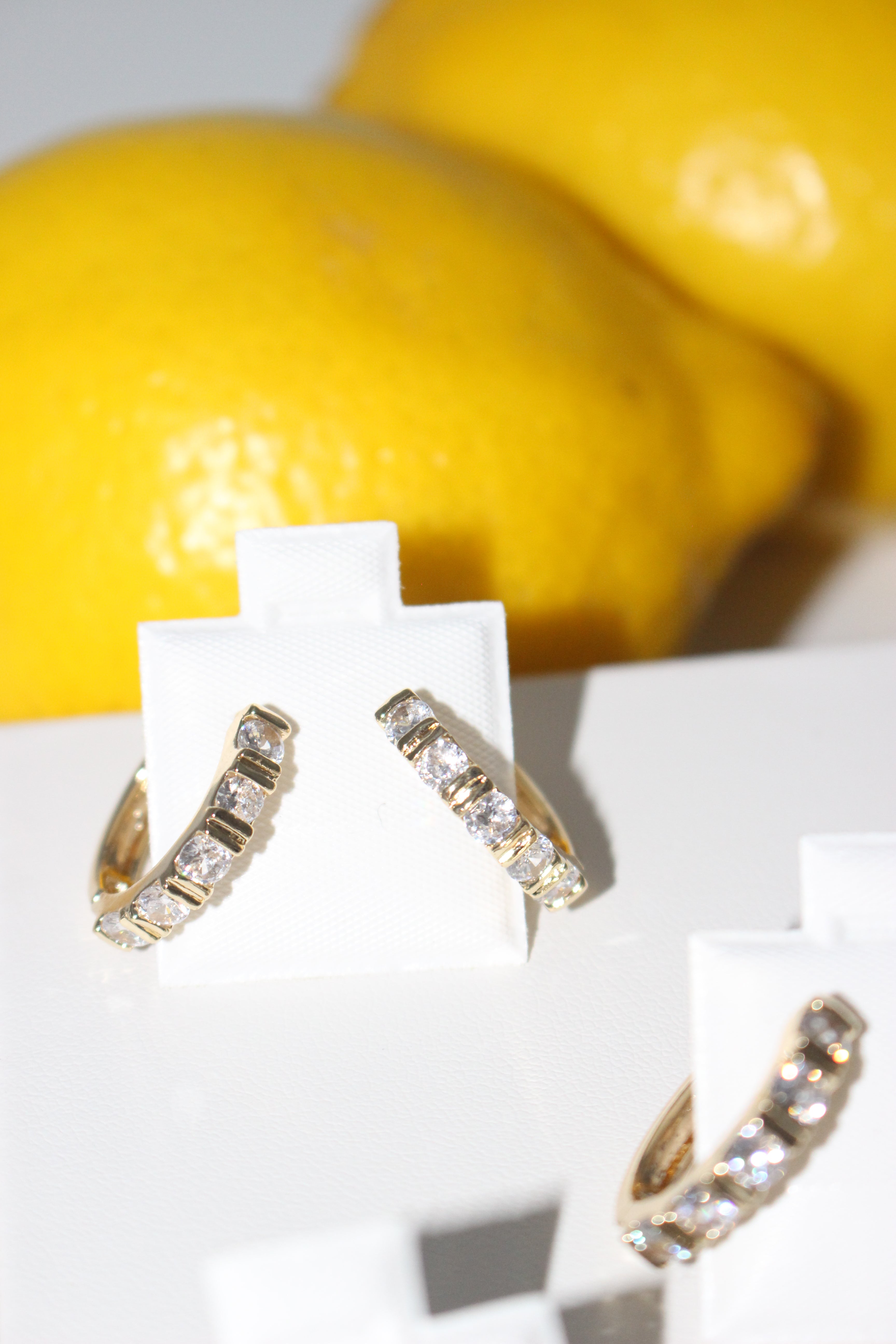 Gold earrings with gemstones on a white surface with a yellow background