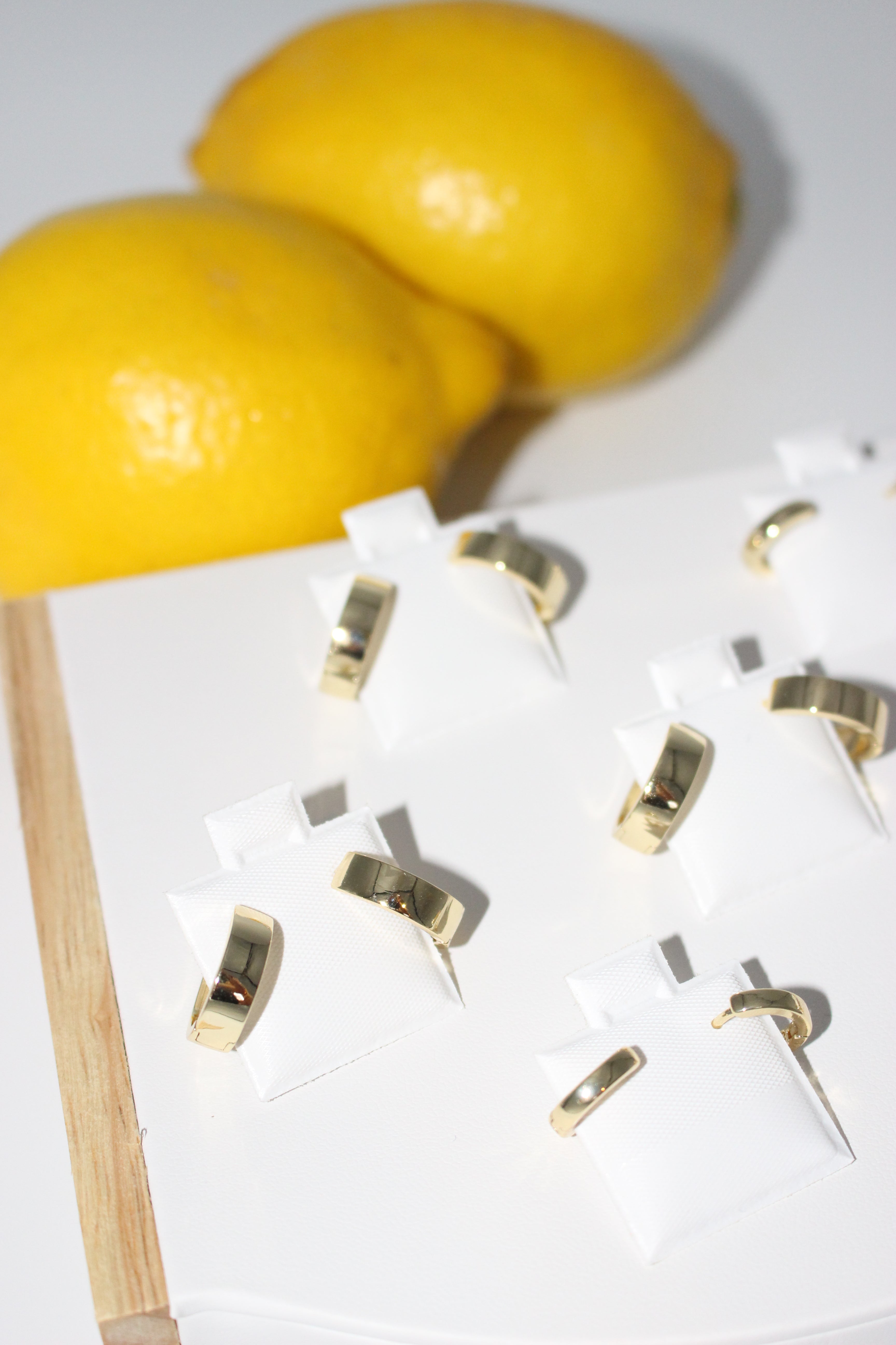 Gold earrings on a white surface with lemons in the background