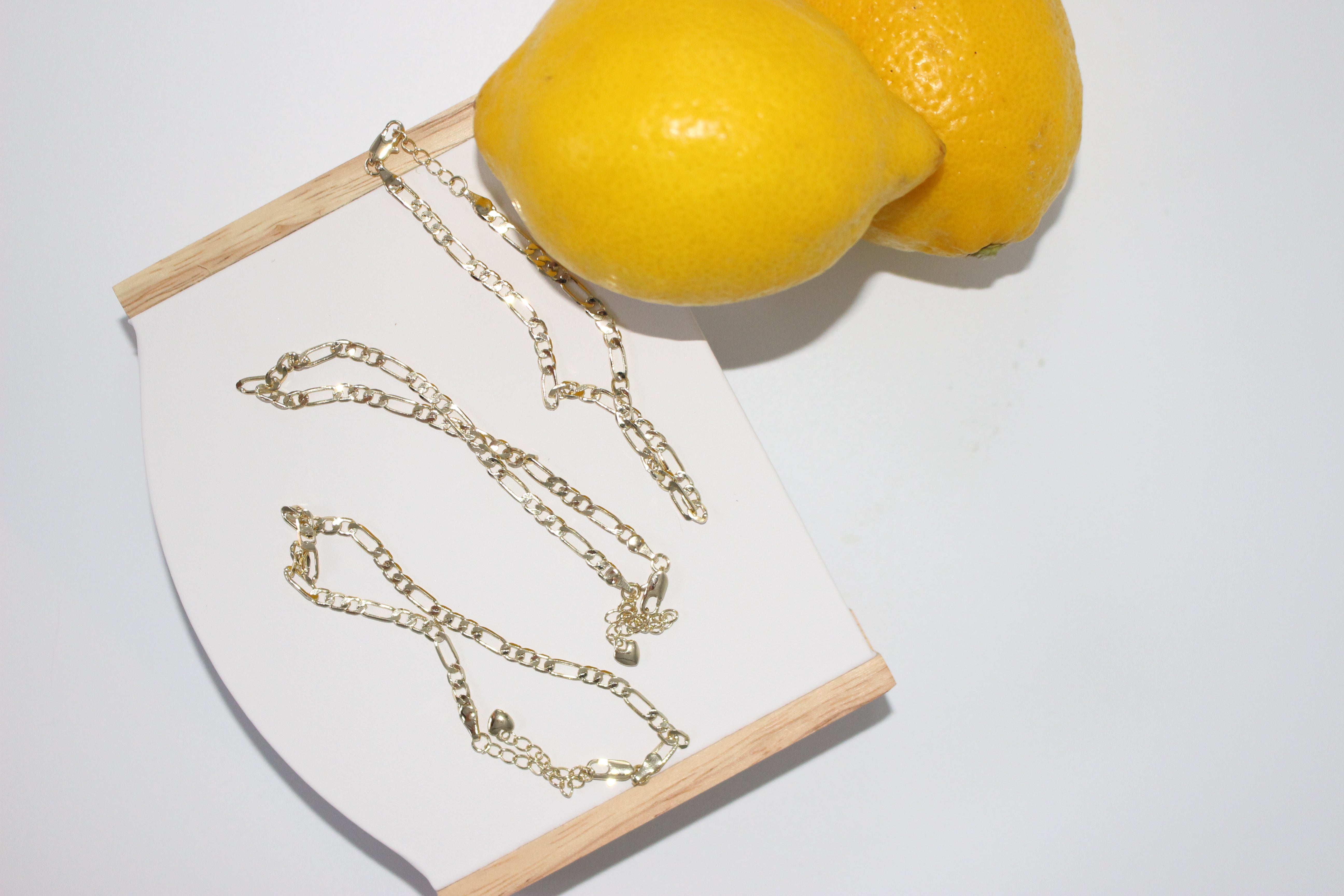 Gold anklets on white surface with lemons in the background