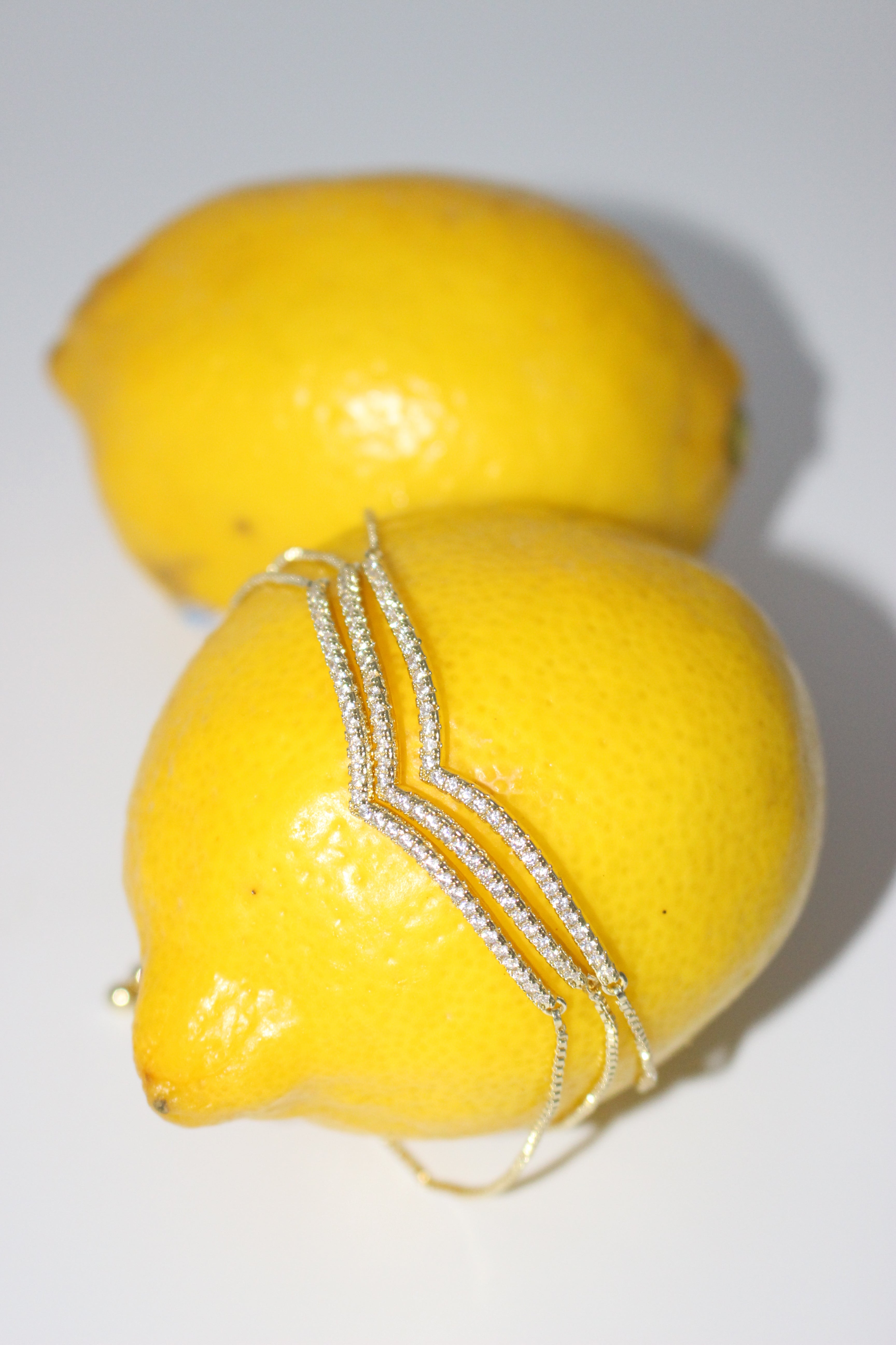 Two lemons with a gold bracelet wrapped around one of them on a white background