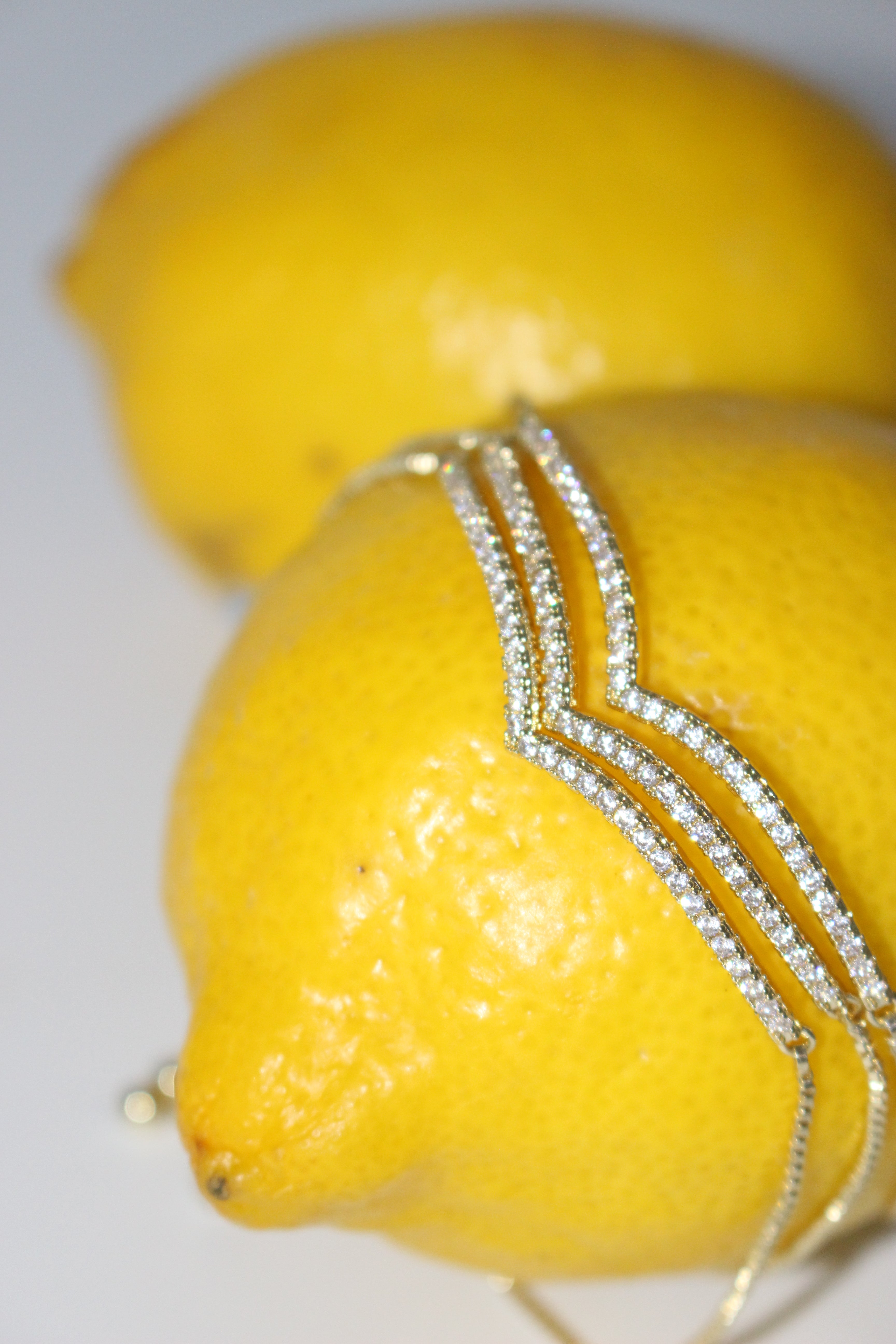 Two lemons with a gold bracelet wrapped around one of them on a white background