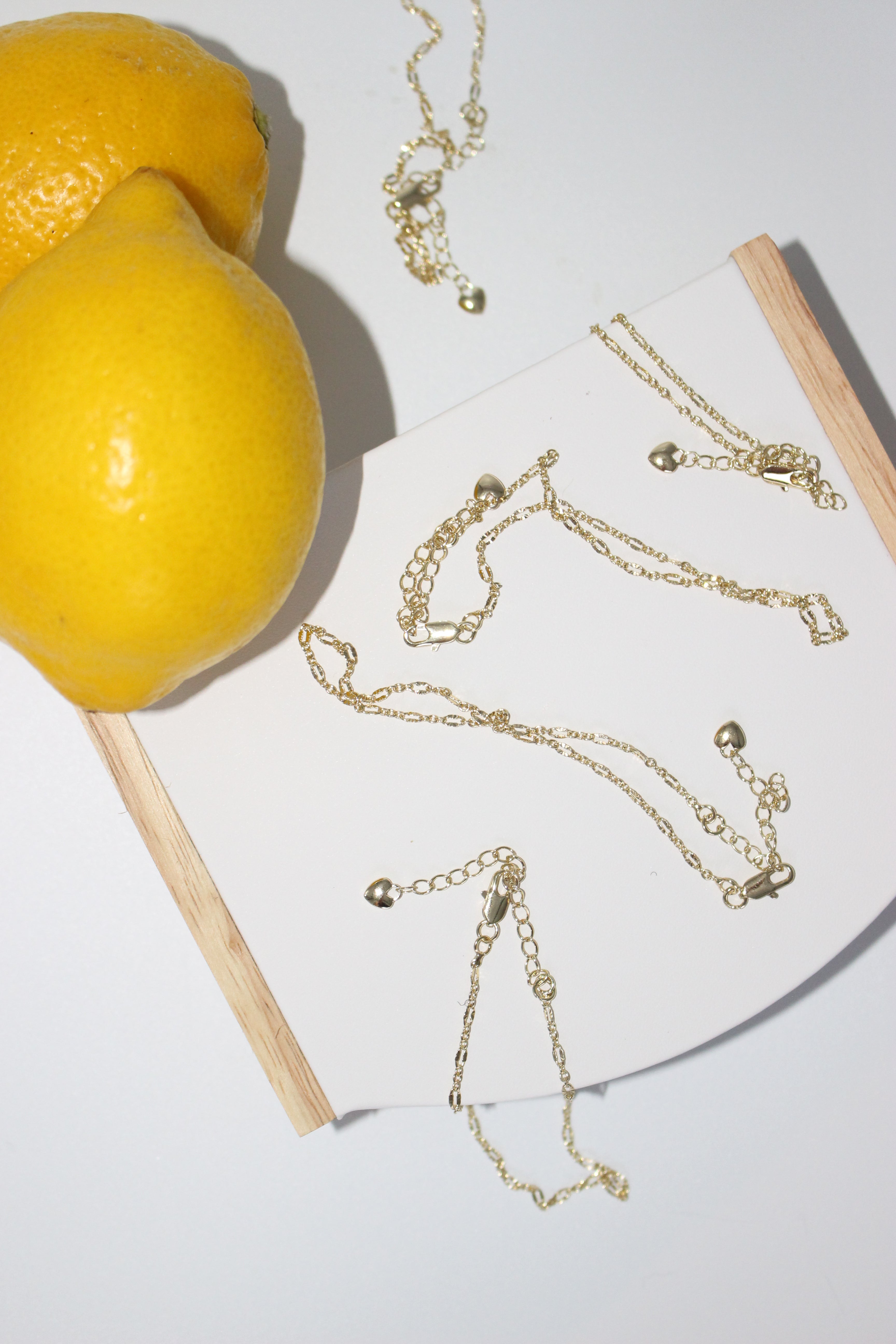 Gold anklets on a white surface with lemons in the background