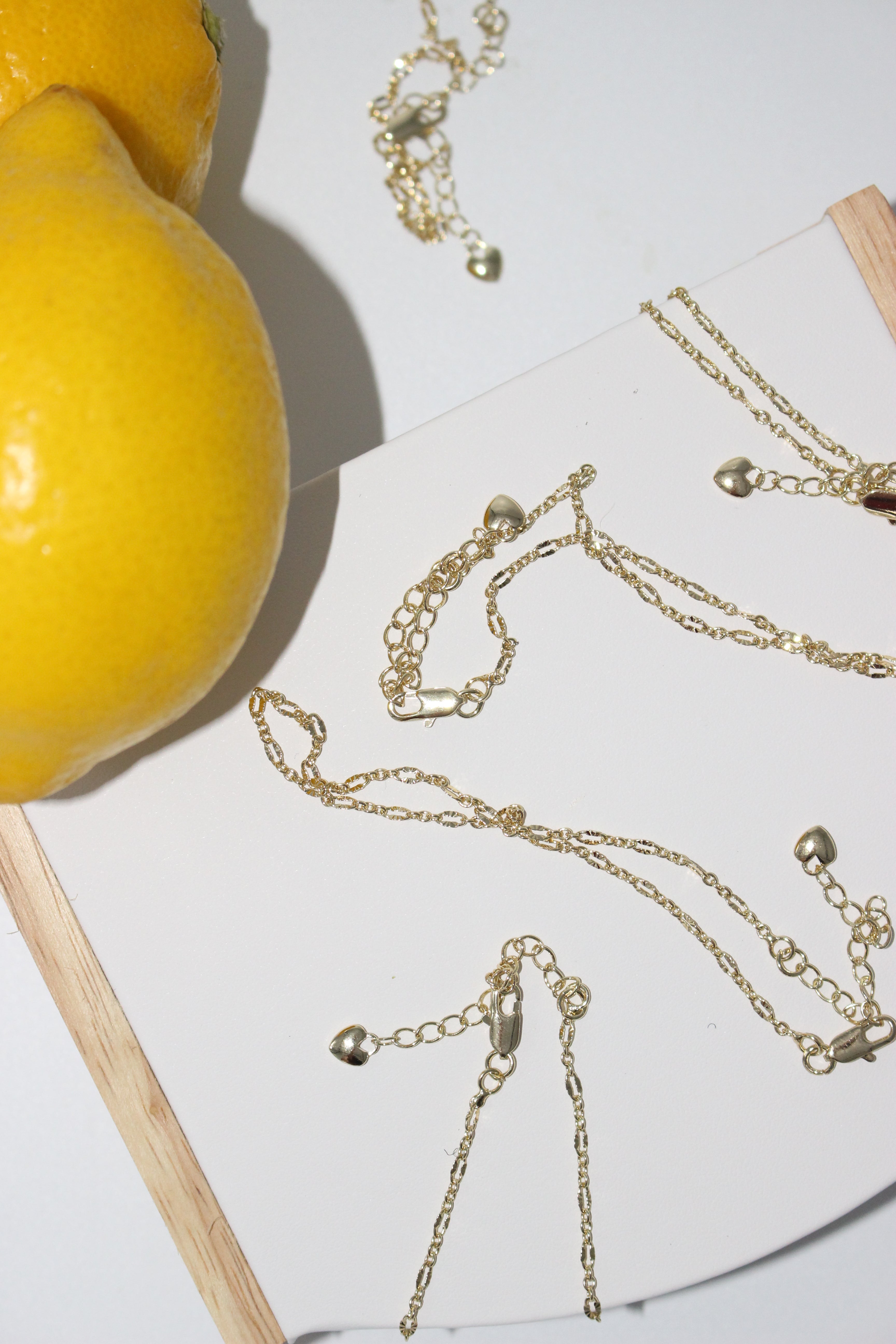 Gold anklets on a white surface with lemons in the background