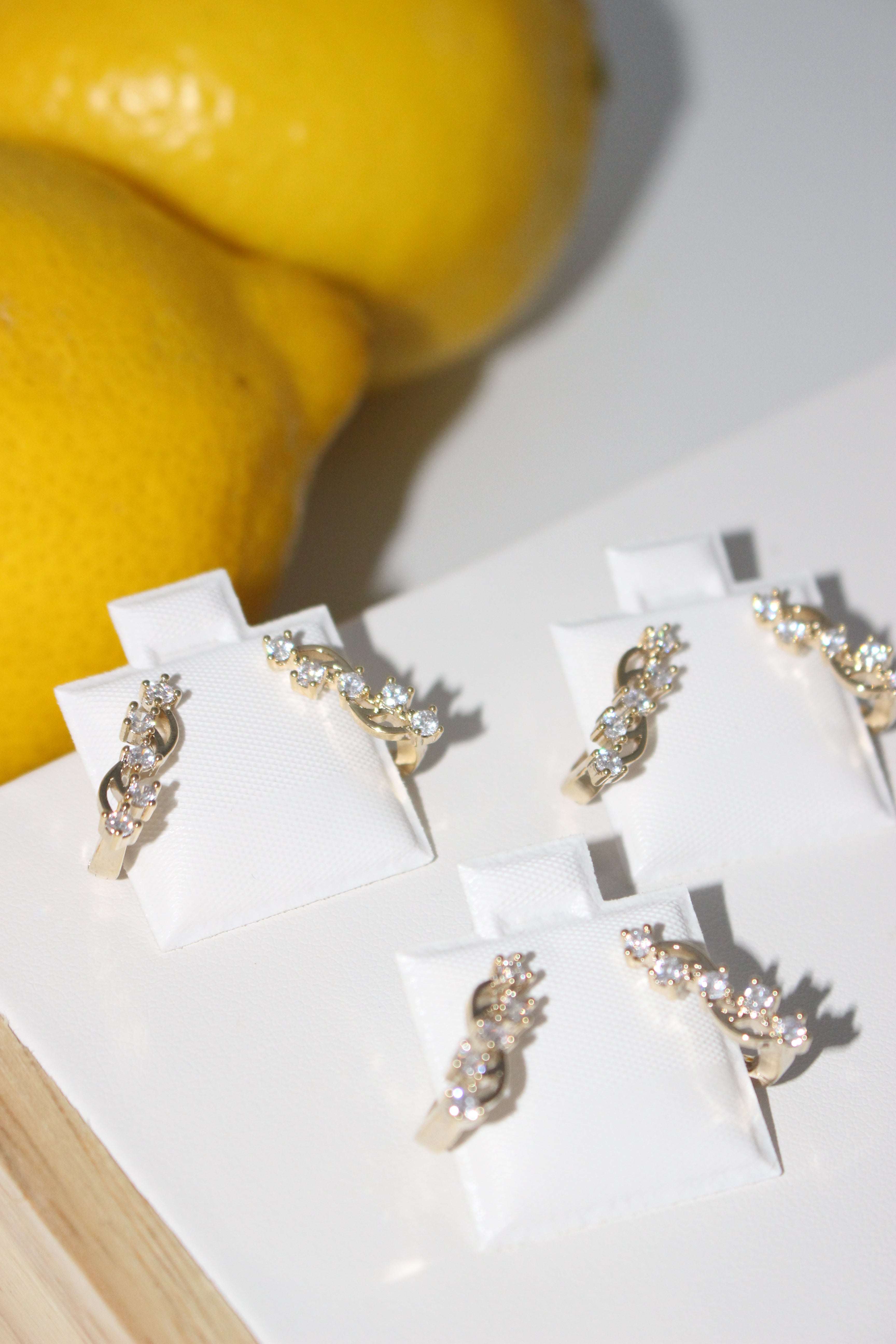 Pair of gold and diamond earrings on a white stand with a yellow fruit in the background.