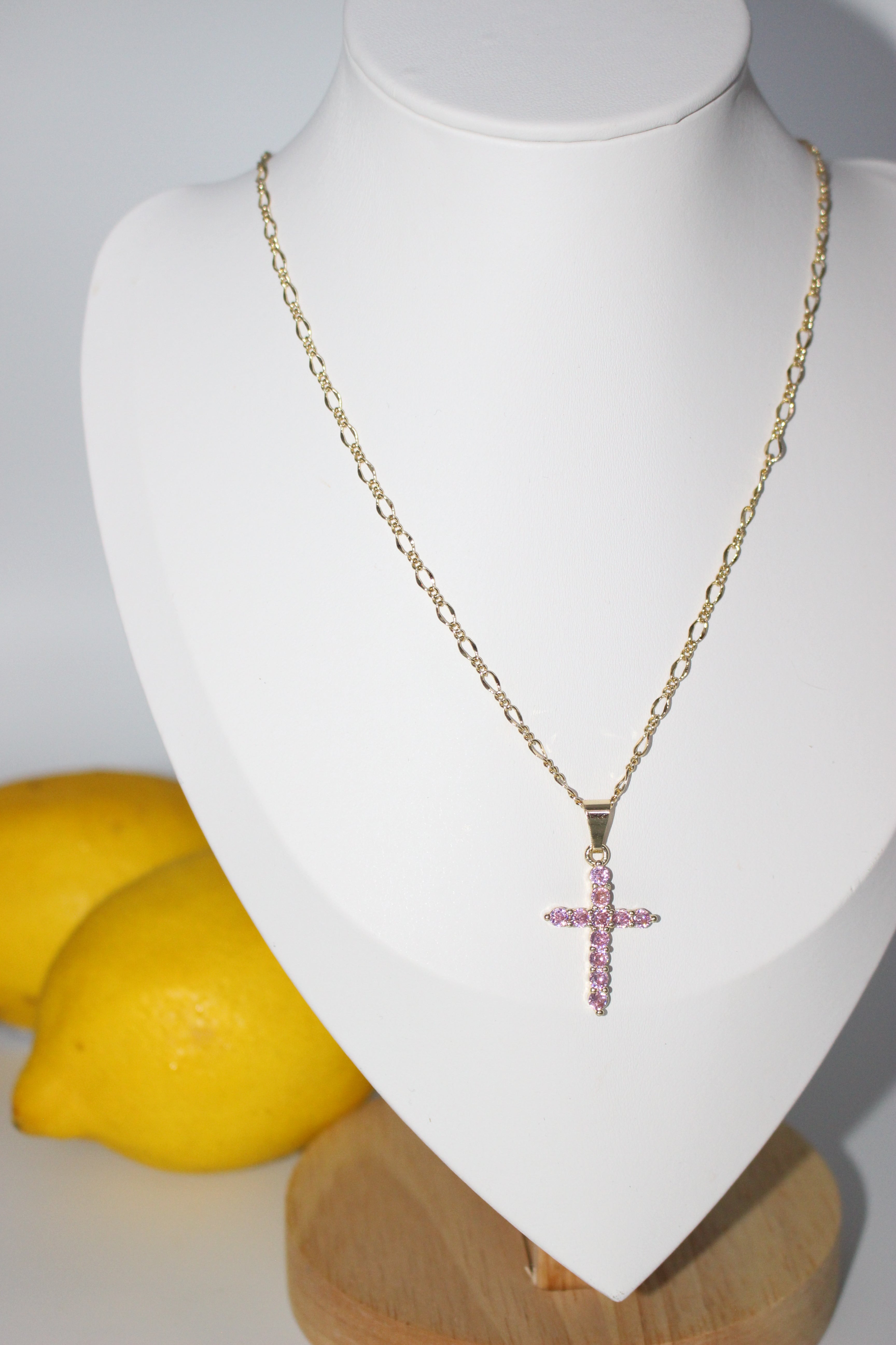 Gold necklace with a cross pendant on a mannequin bust, with lemons in the background.