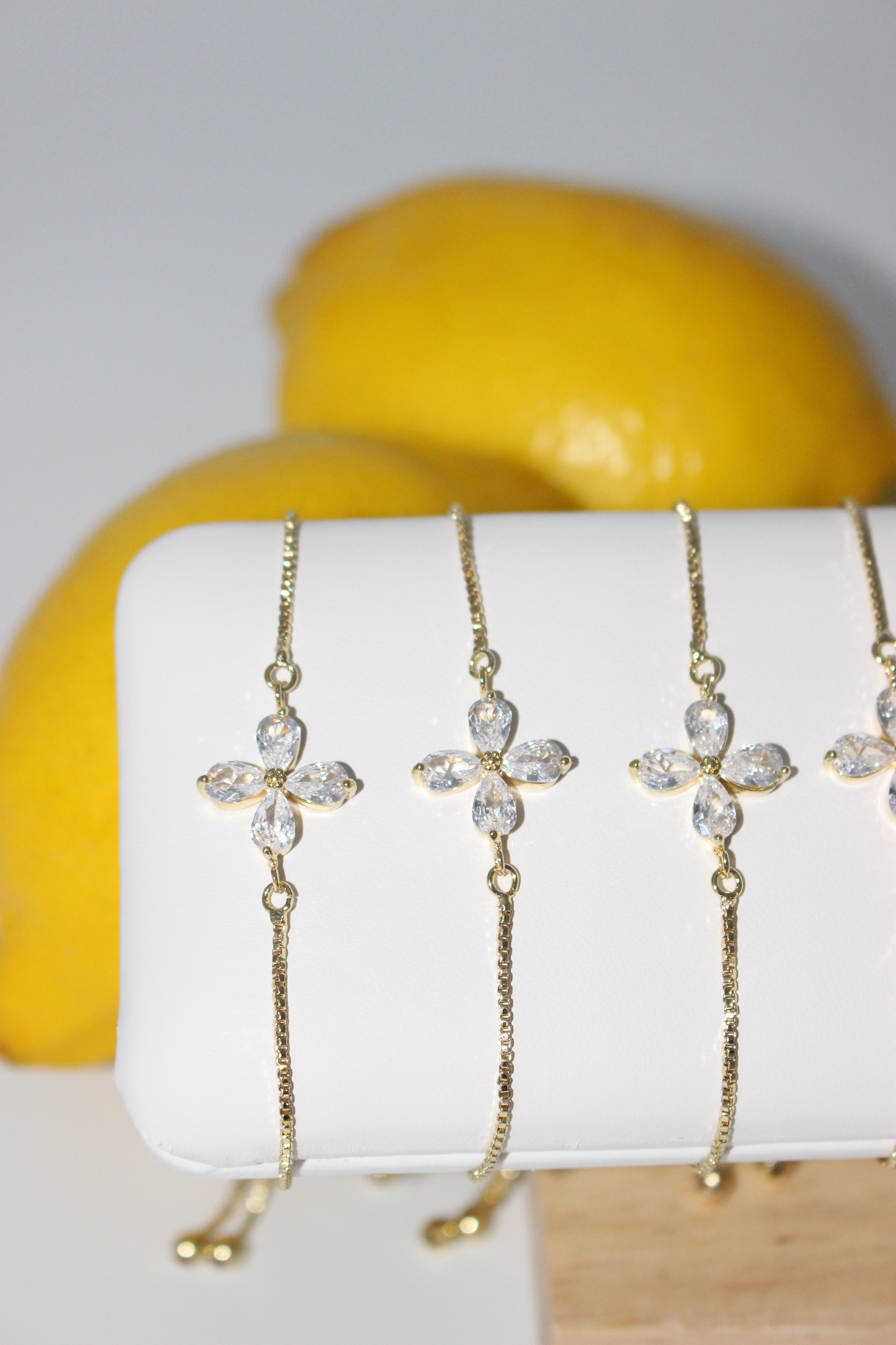 Set of gold bracelets with crystals on a white cylindrical stand against a yellow background