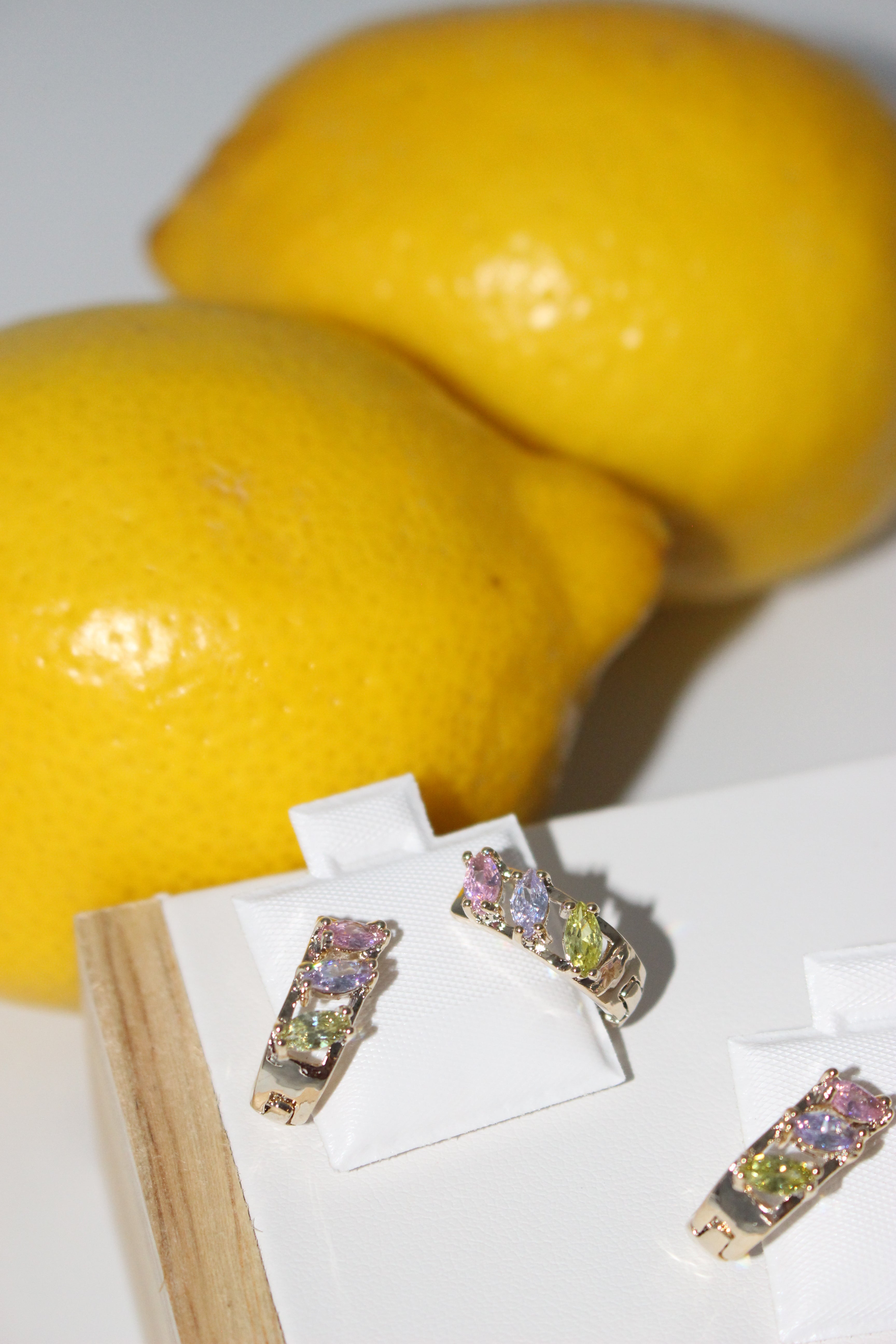 Colorful gem huggie hoops on white surface with lemons in background