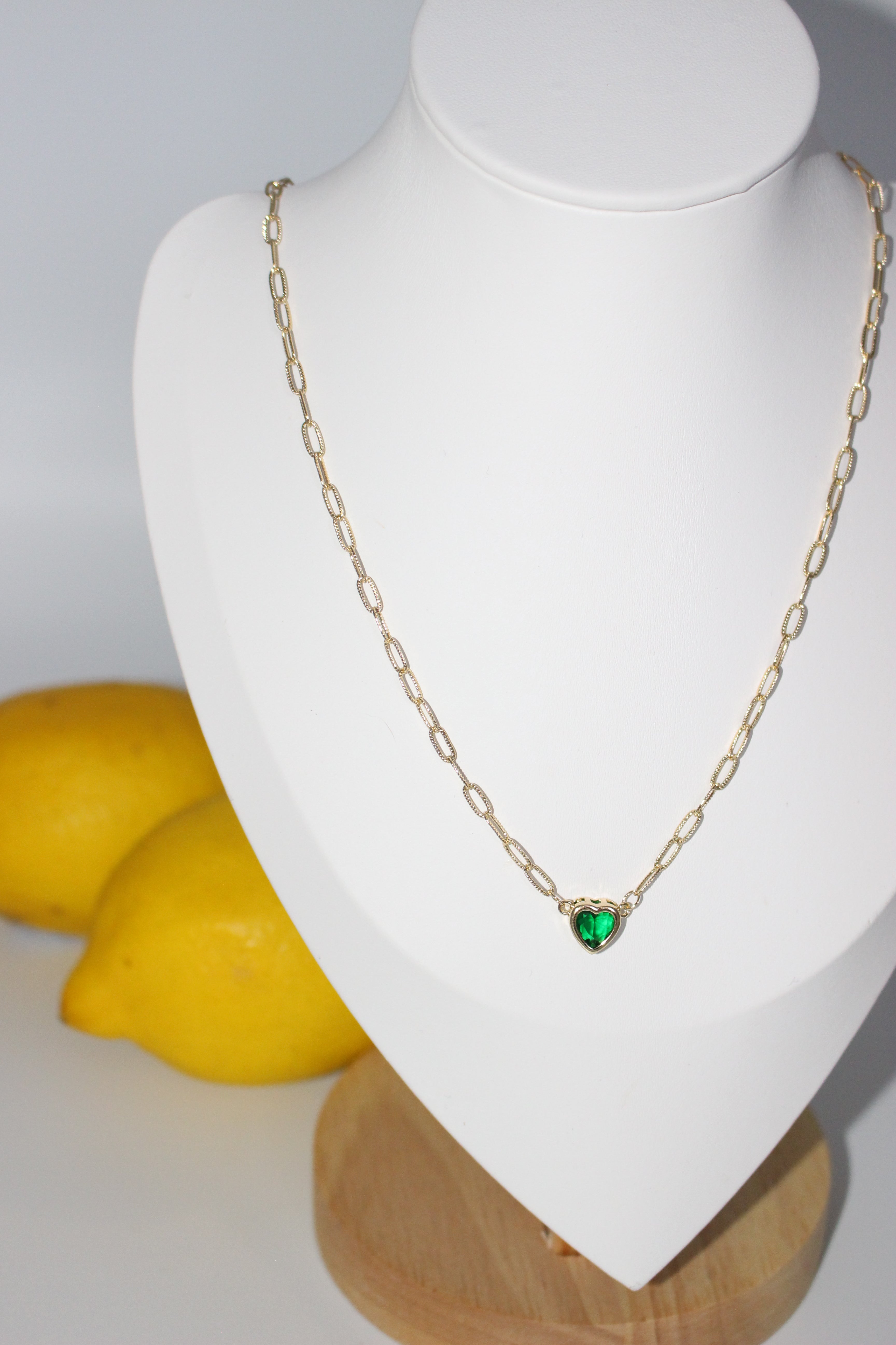 Gold necklace with a green gemstone on a mannequin bust against a white background.