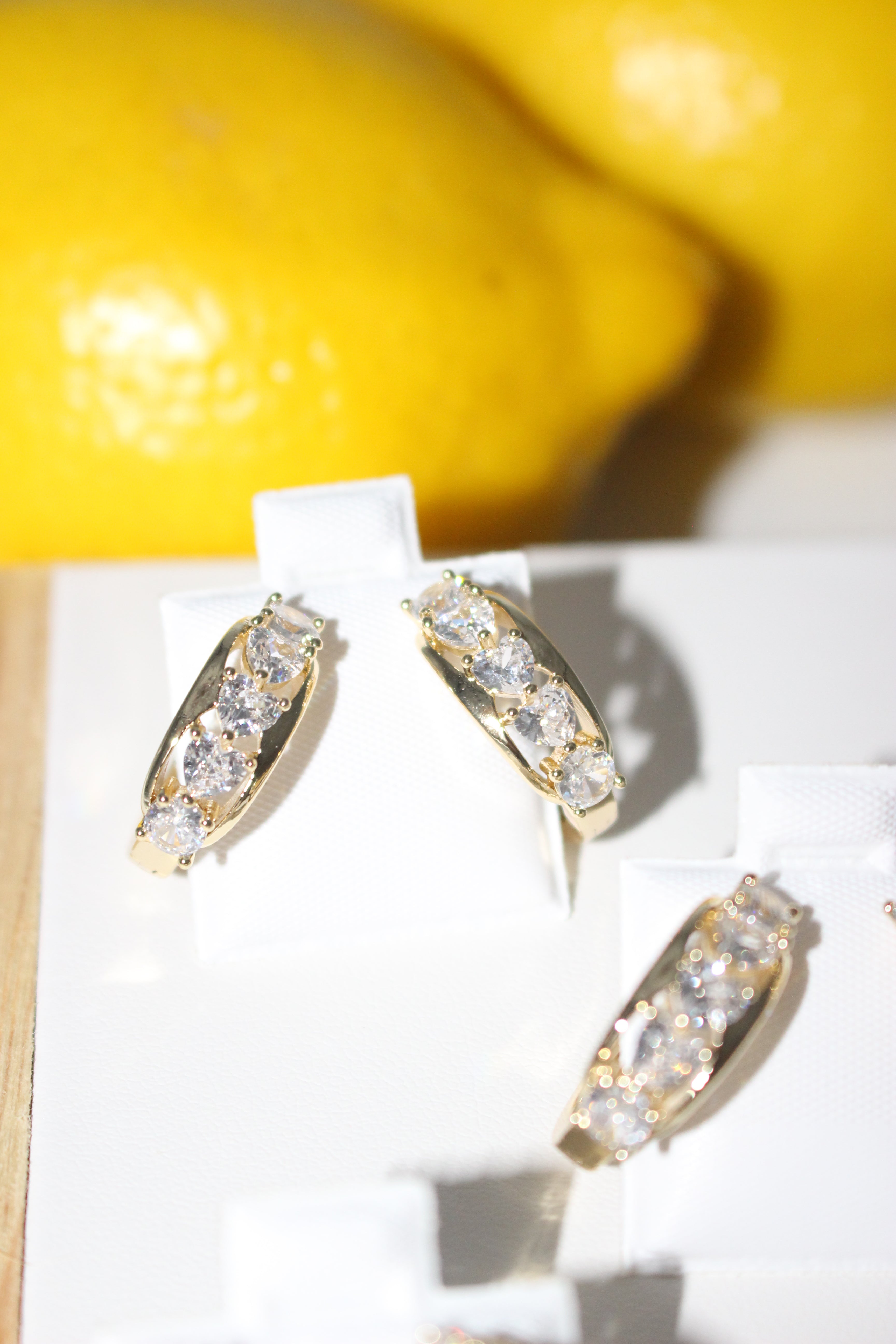 Gold hoop earrings with clear stones on a white surface with a yellow background
