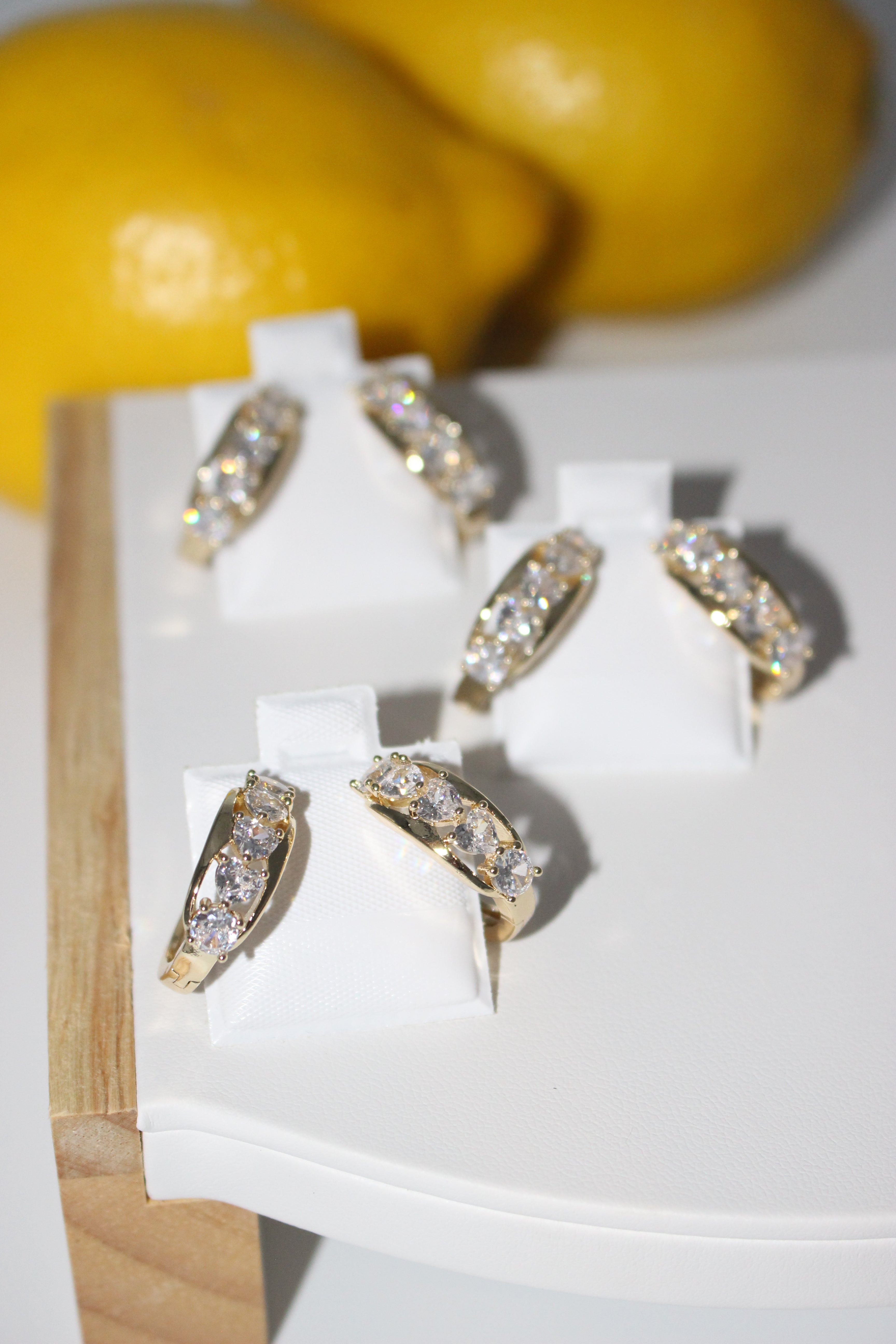 Gold and diamond earrings on a white stand with a yellow fruit in the background