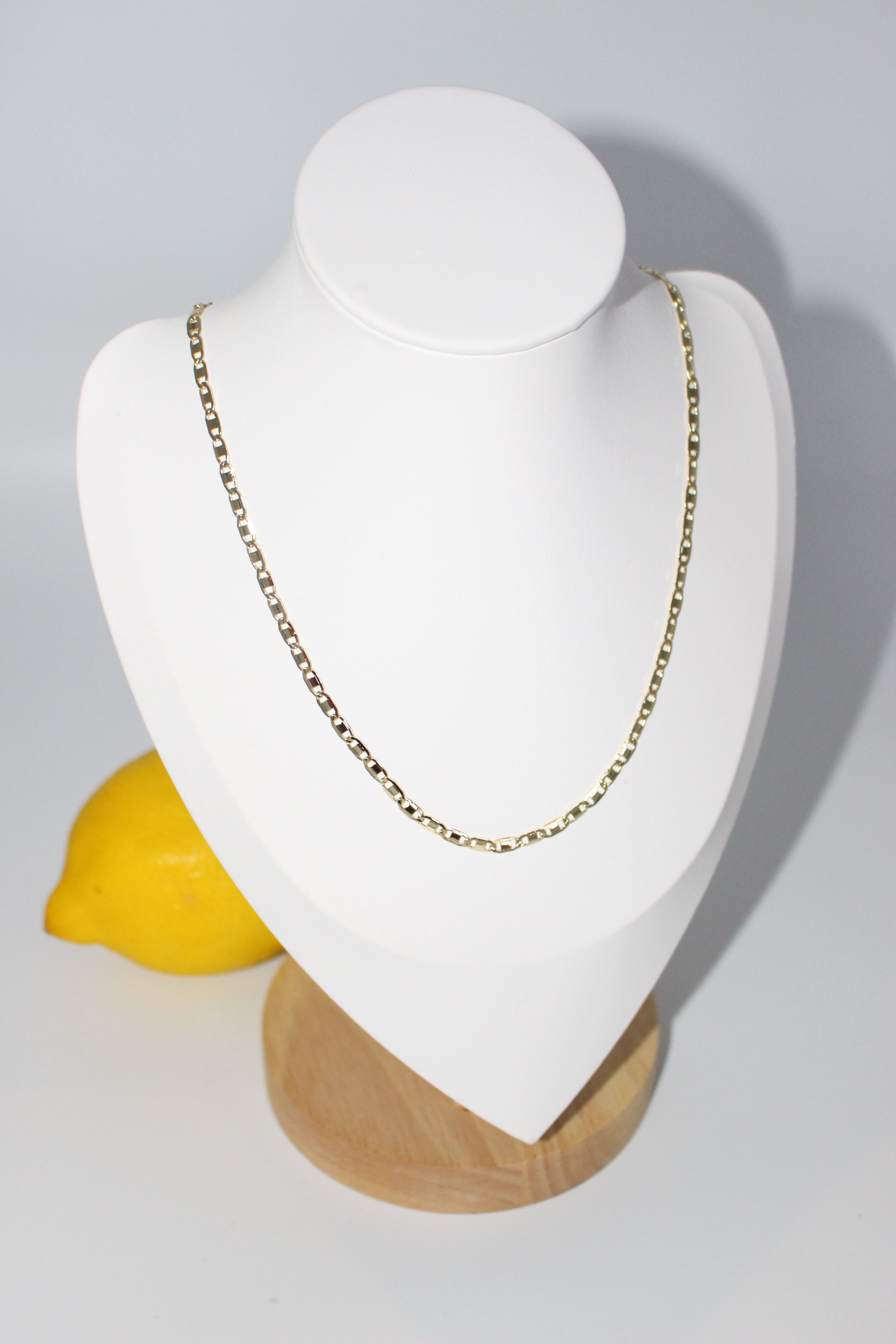 Gold necklace on white stand with lemons in the background.