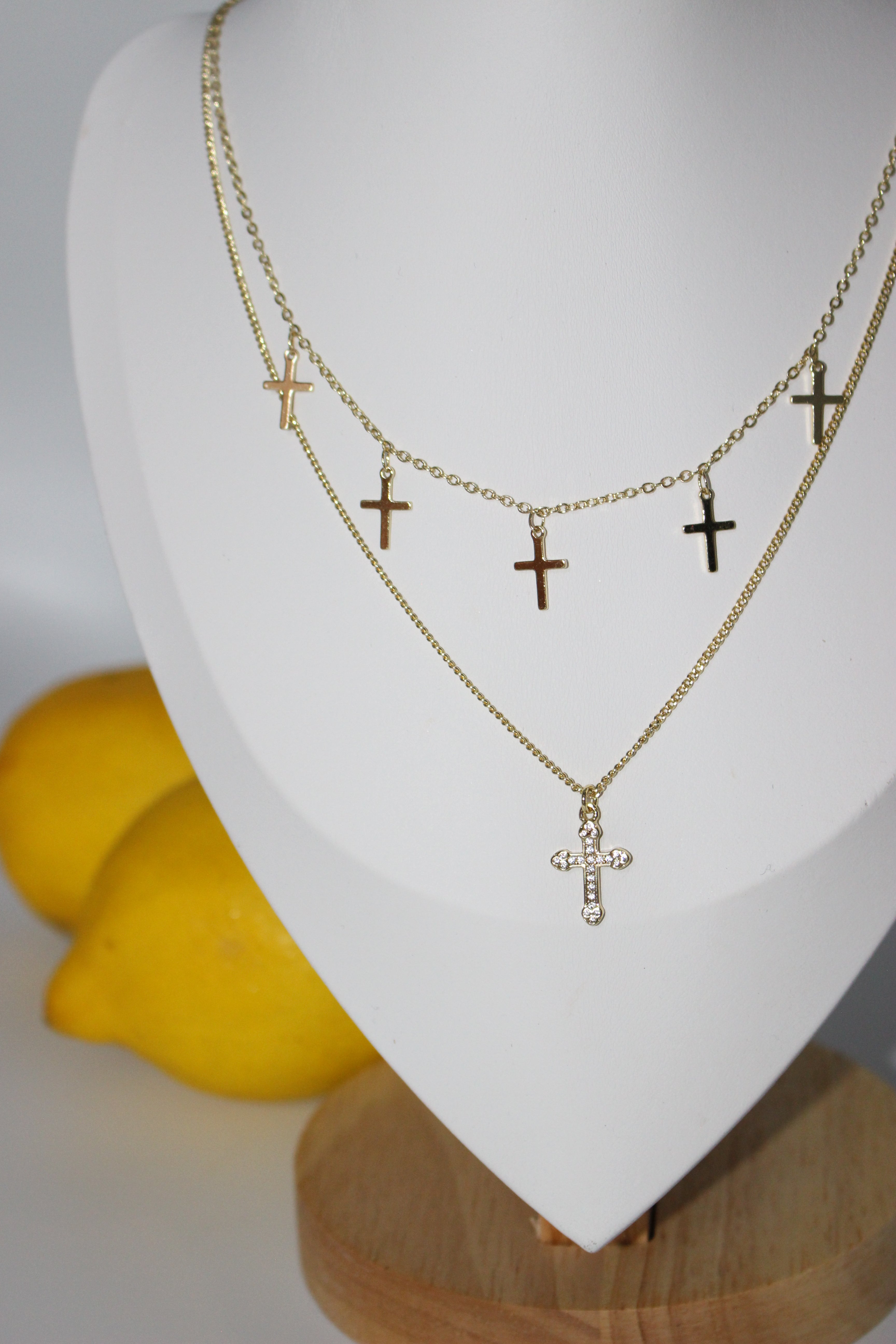 Gold necklaces with cross pendants on a white stand with lemons in the background