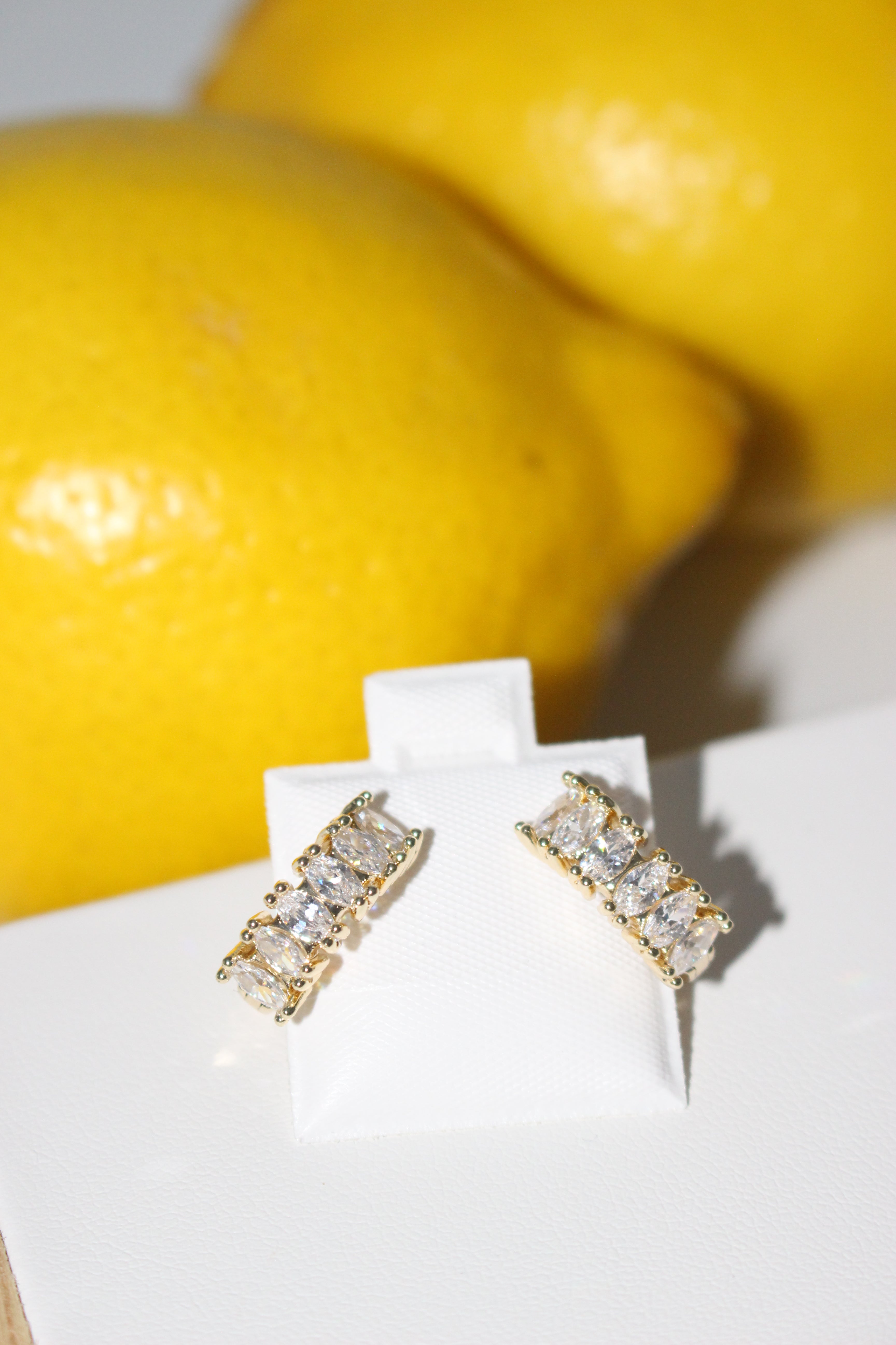 Gold and diamond earrings on a white card with lemons in the background