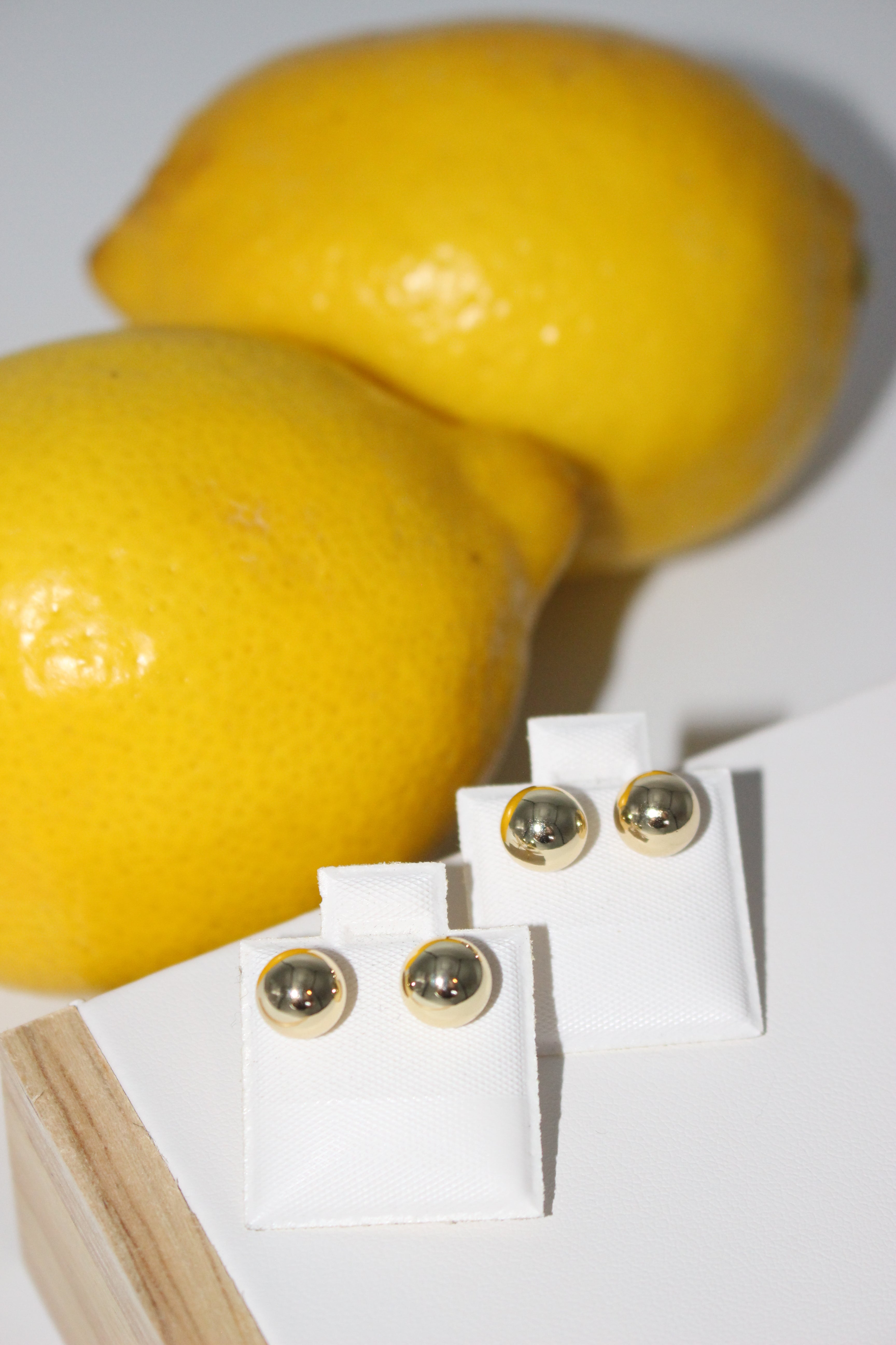 Gold studs on a white card, next to two lemons on a white background