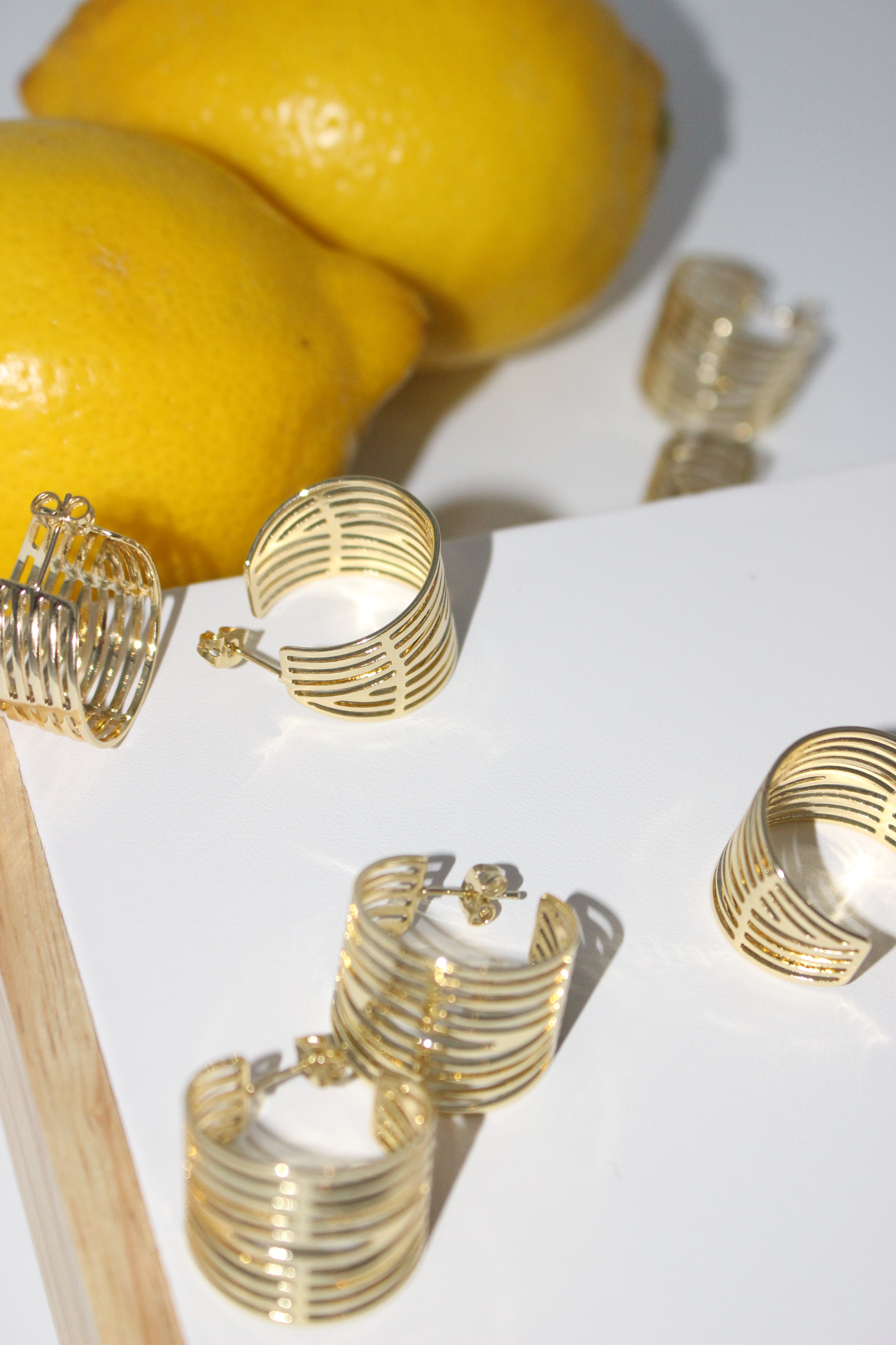 Gold hoop earrings on a white surface with a lemon in the background