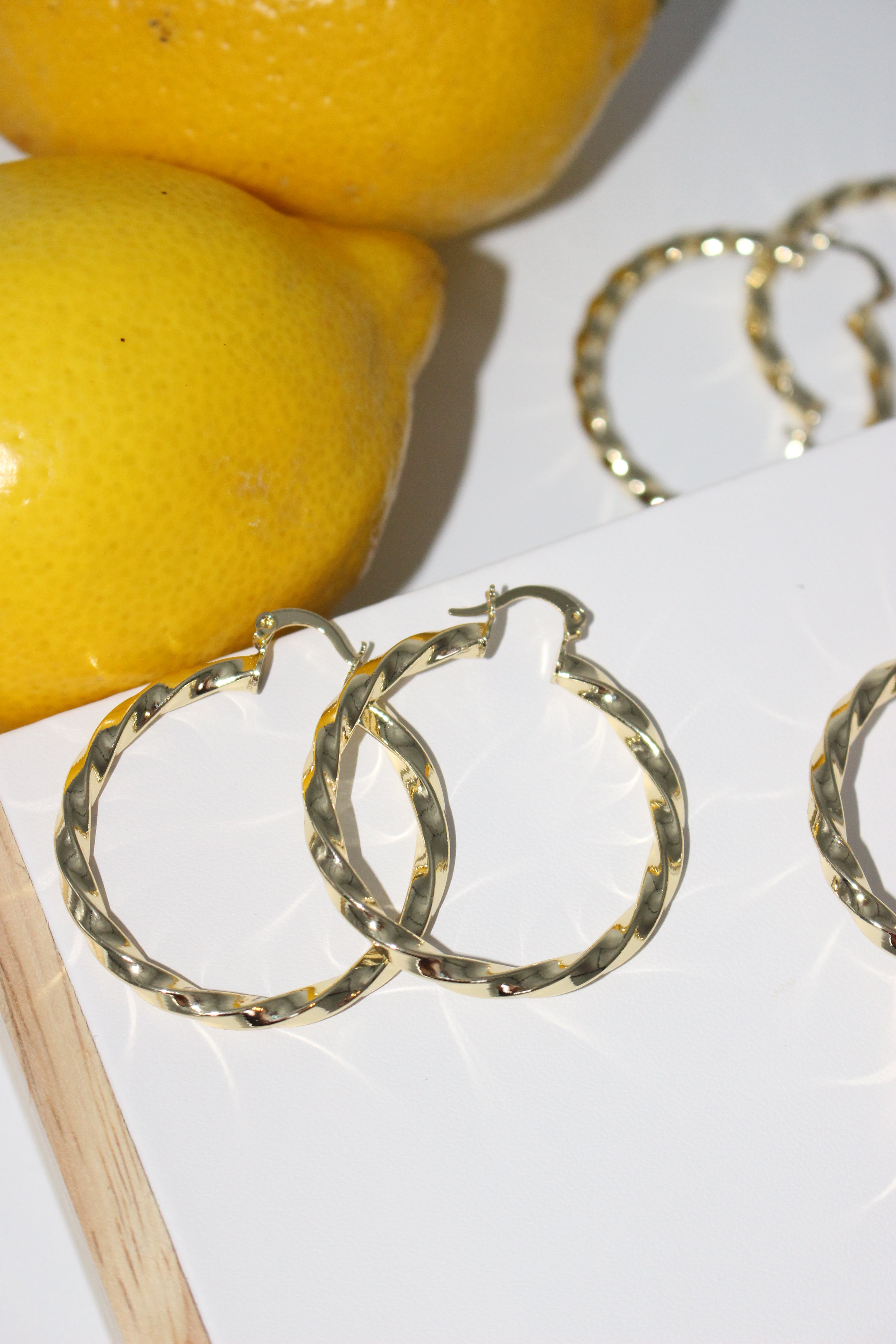 Gold hoop earrings on a white surface with lemons in the background