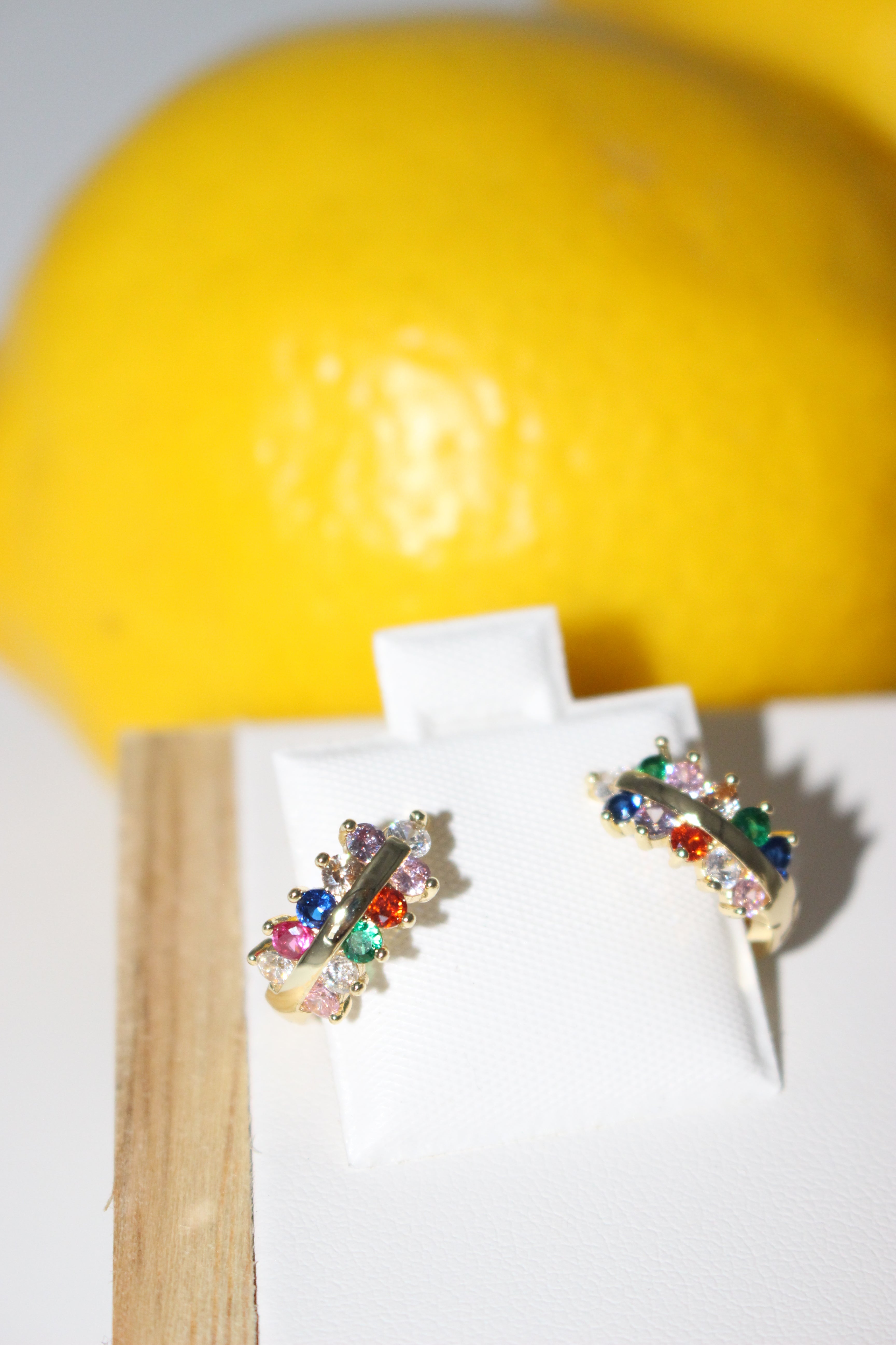 Colorful gemstone earrings on a white box with a yellow fruit in the background