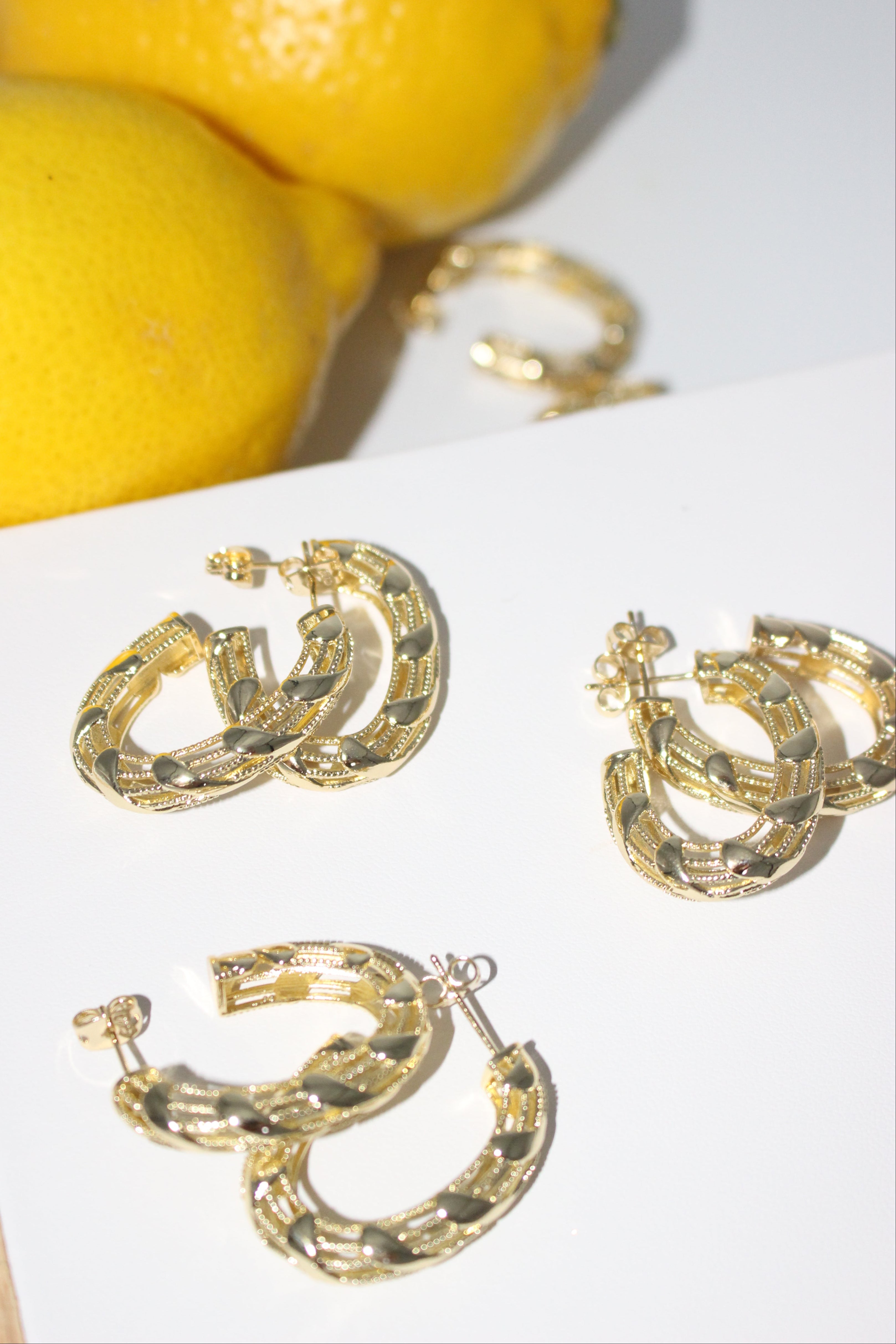 Gold hoop earrings on a white surface with lemons in the background