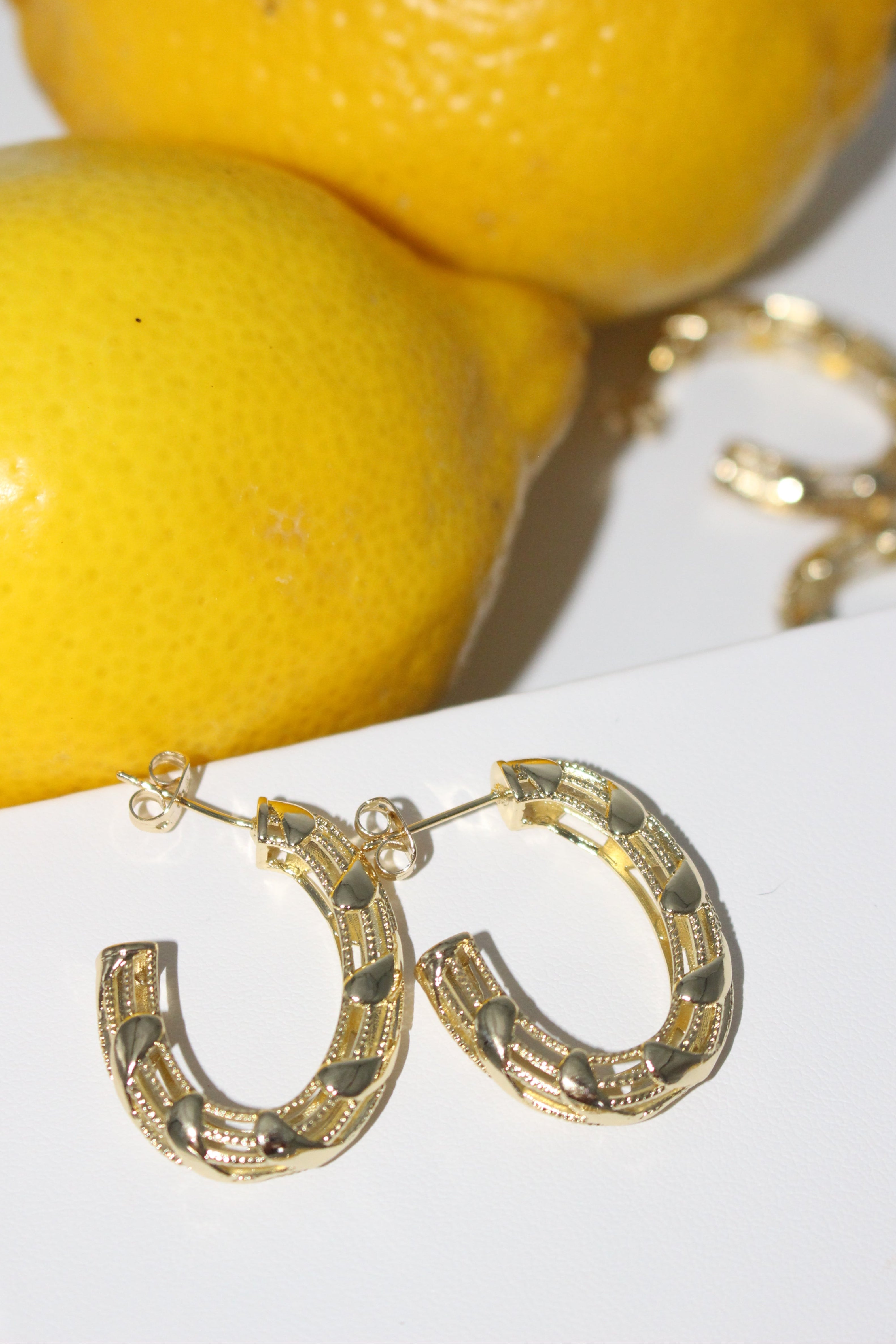 Gold hoop earrings next to two lemons on a white surface