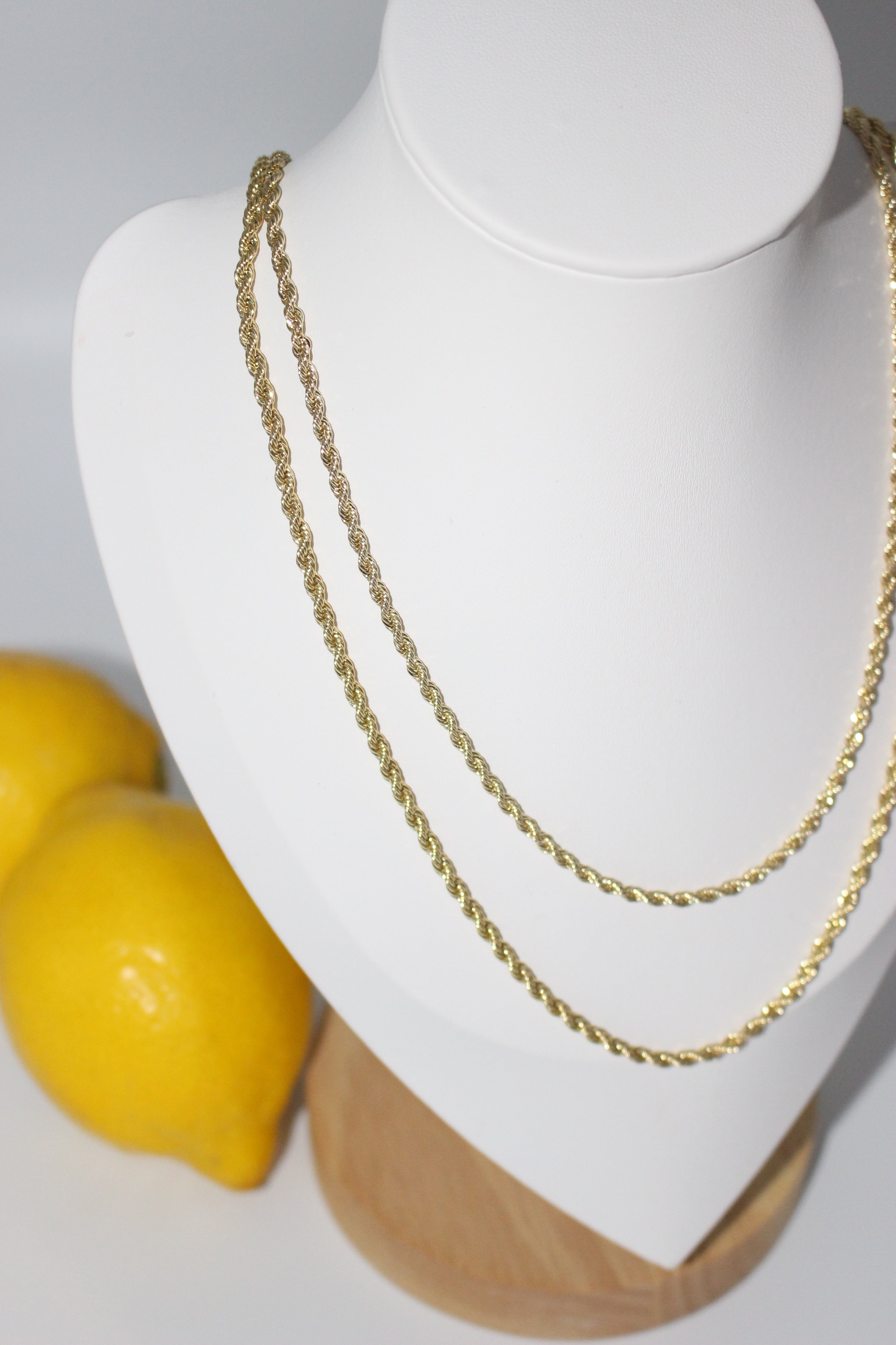 Gold necklaces on a mannequin bust with lemons in the background