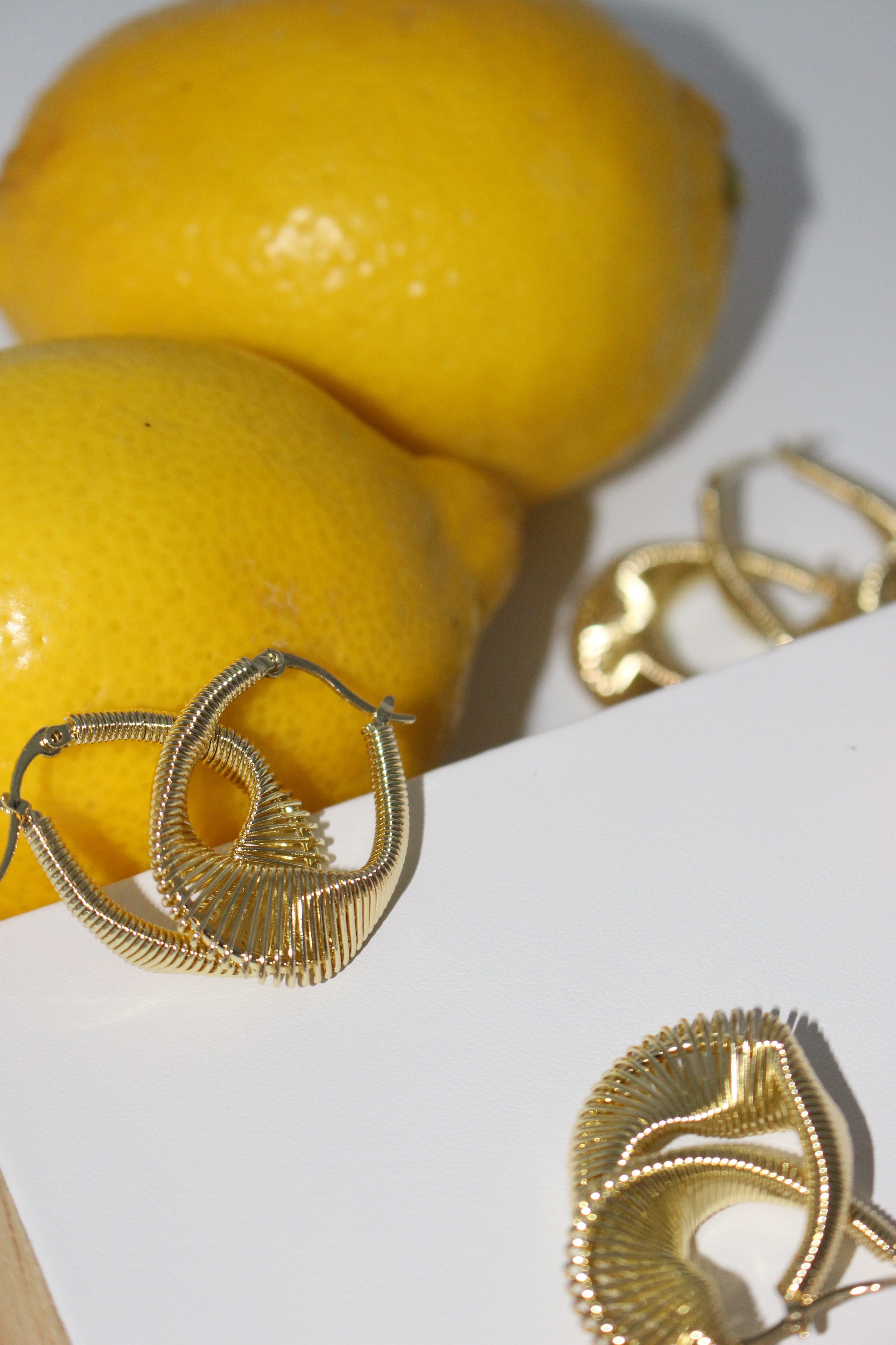 Gold earrings with leaf design on a white surface with lemons.