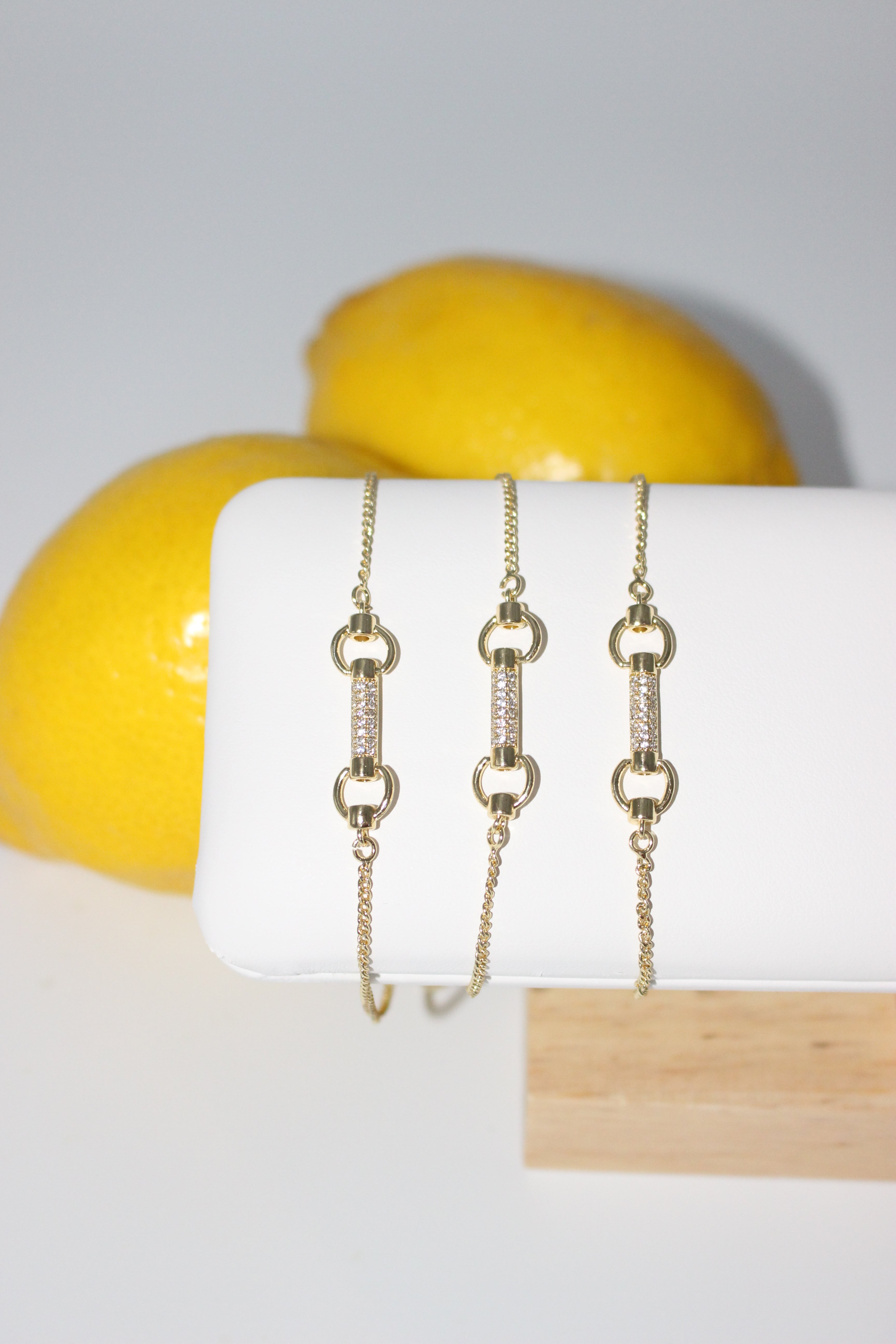 Gold bracelets on a white surface with lemons in the background