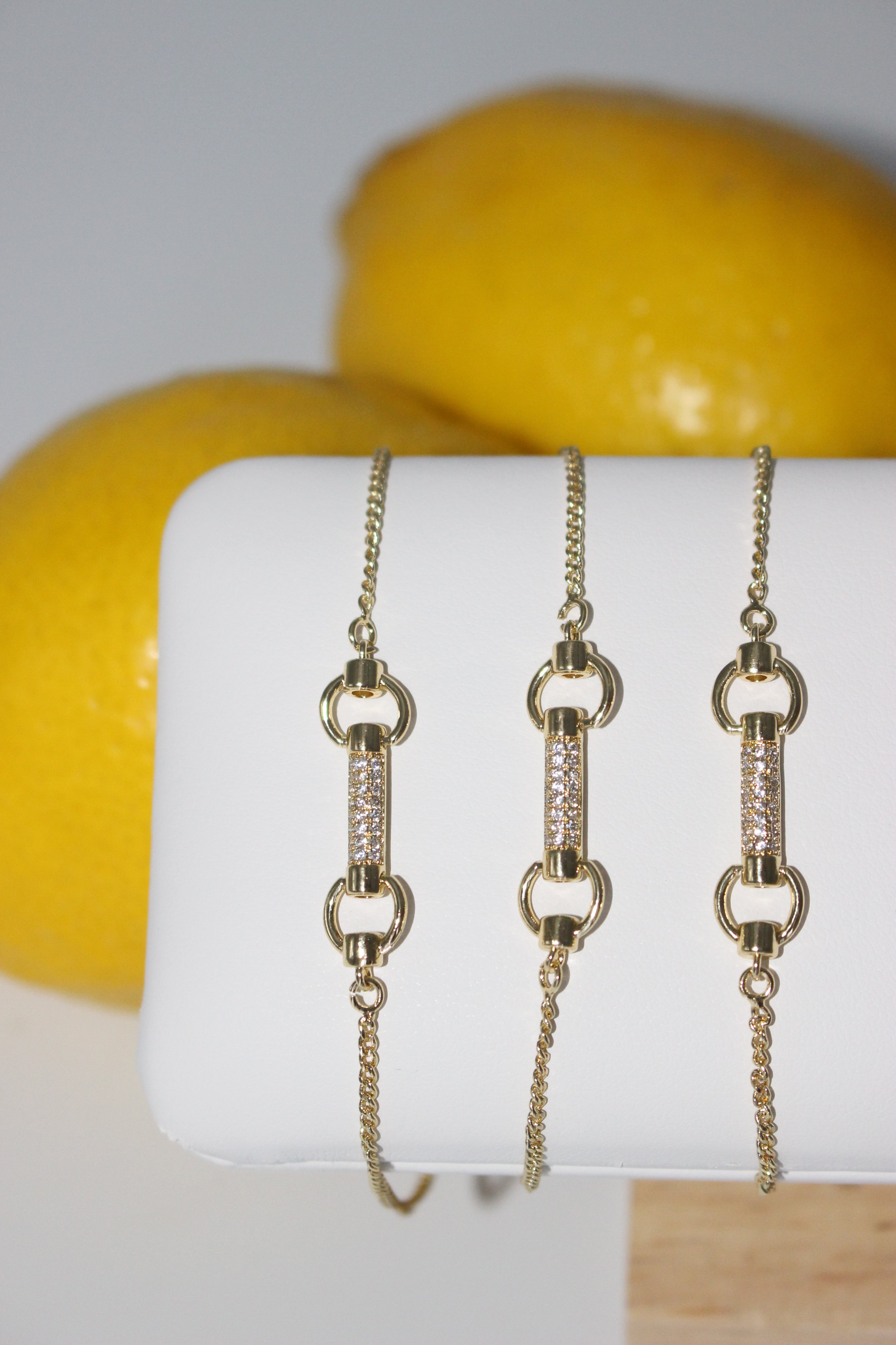 Gold bracelets on a white surface with lemons in the background