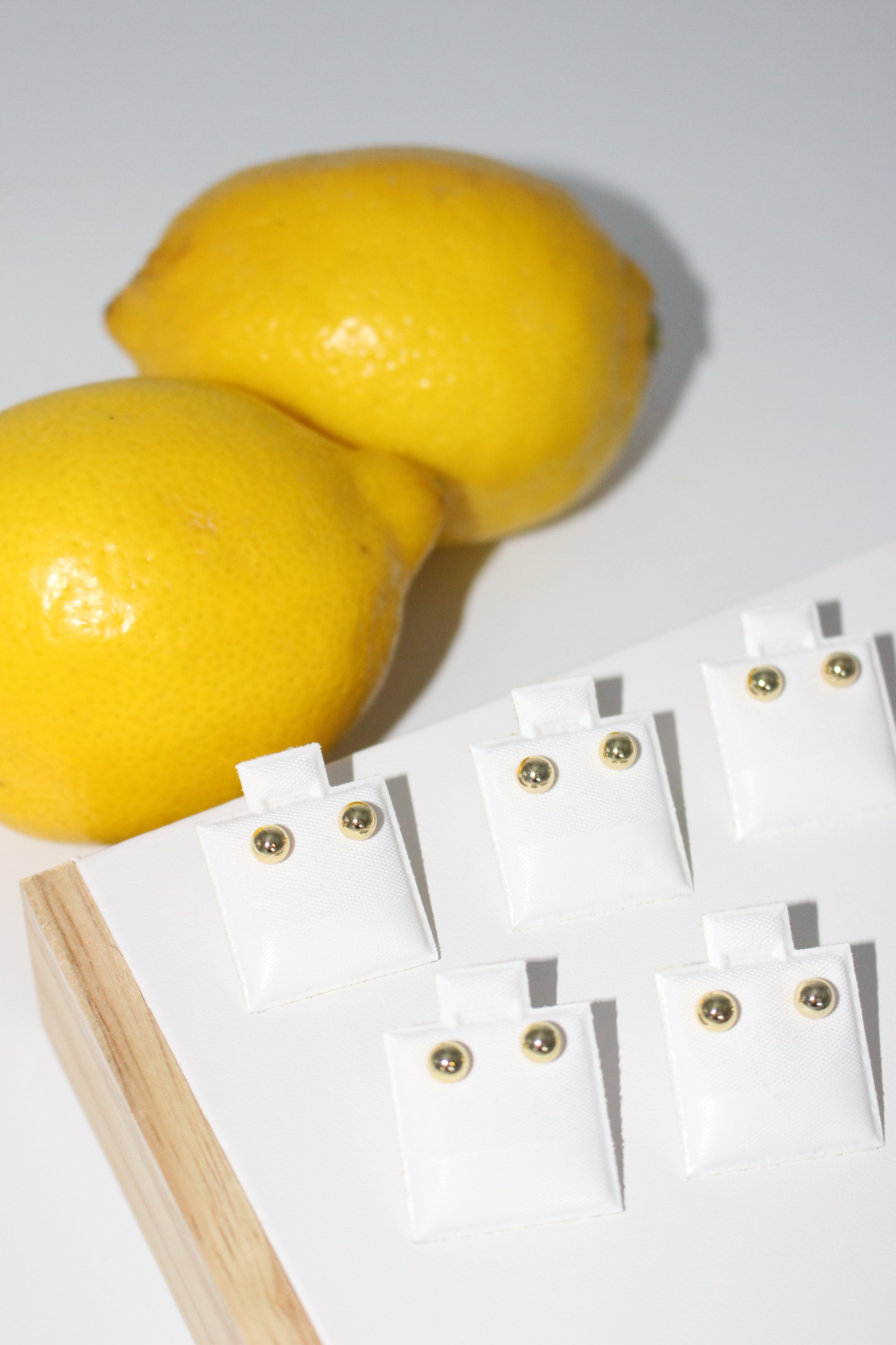 Gold studs on a white card, next to two lemons on a white background