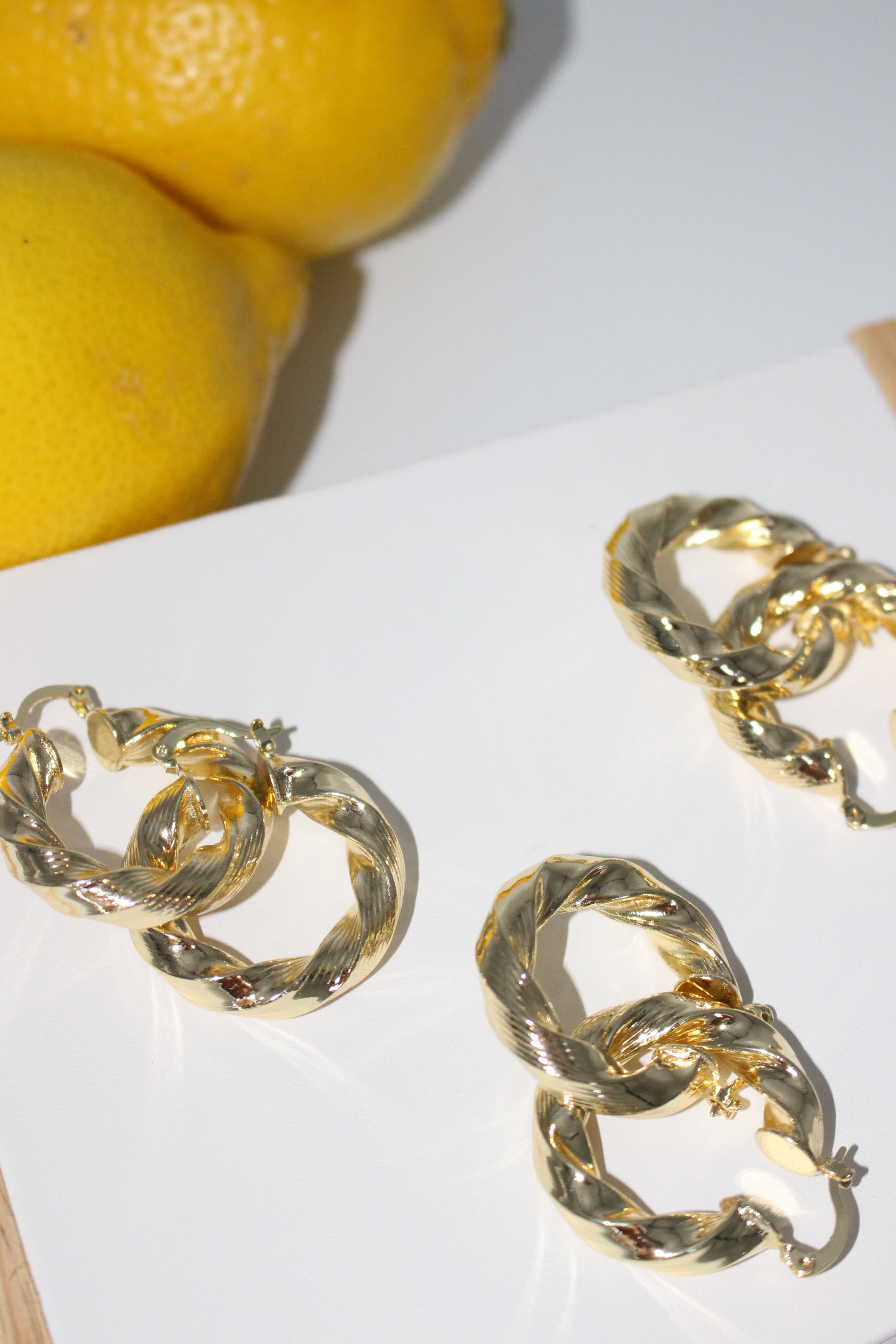 Gold hoop earrings on a white surface with lemons in the background