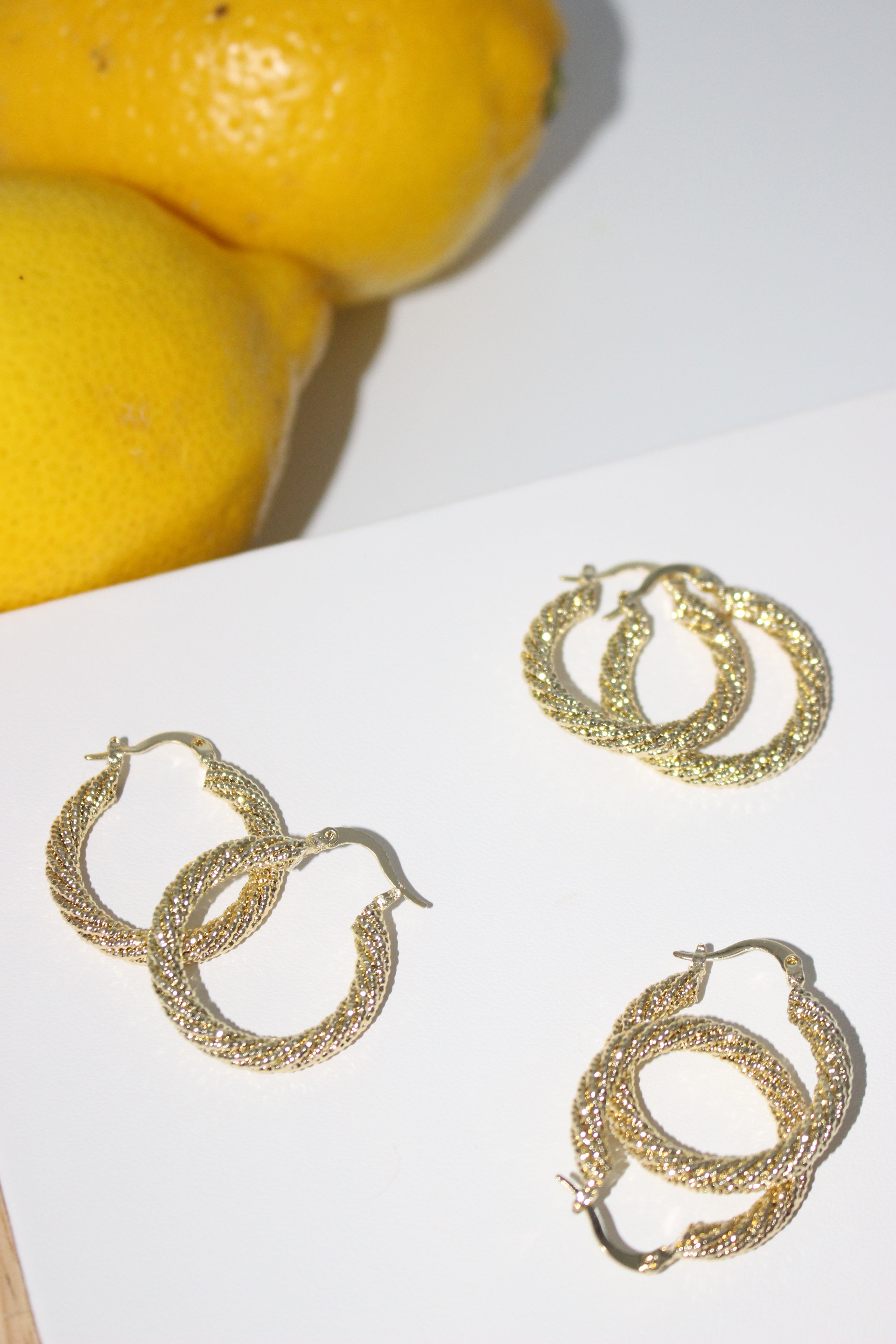 Gold hoop earrings on a white surface with lemons in the background