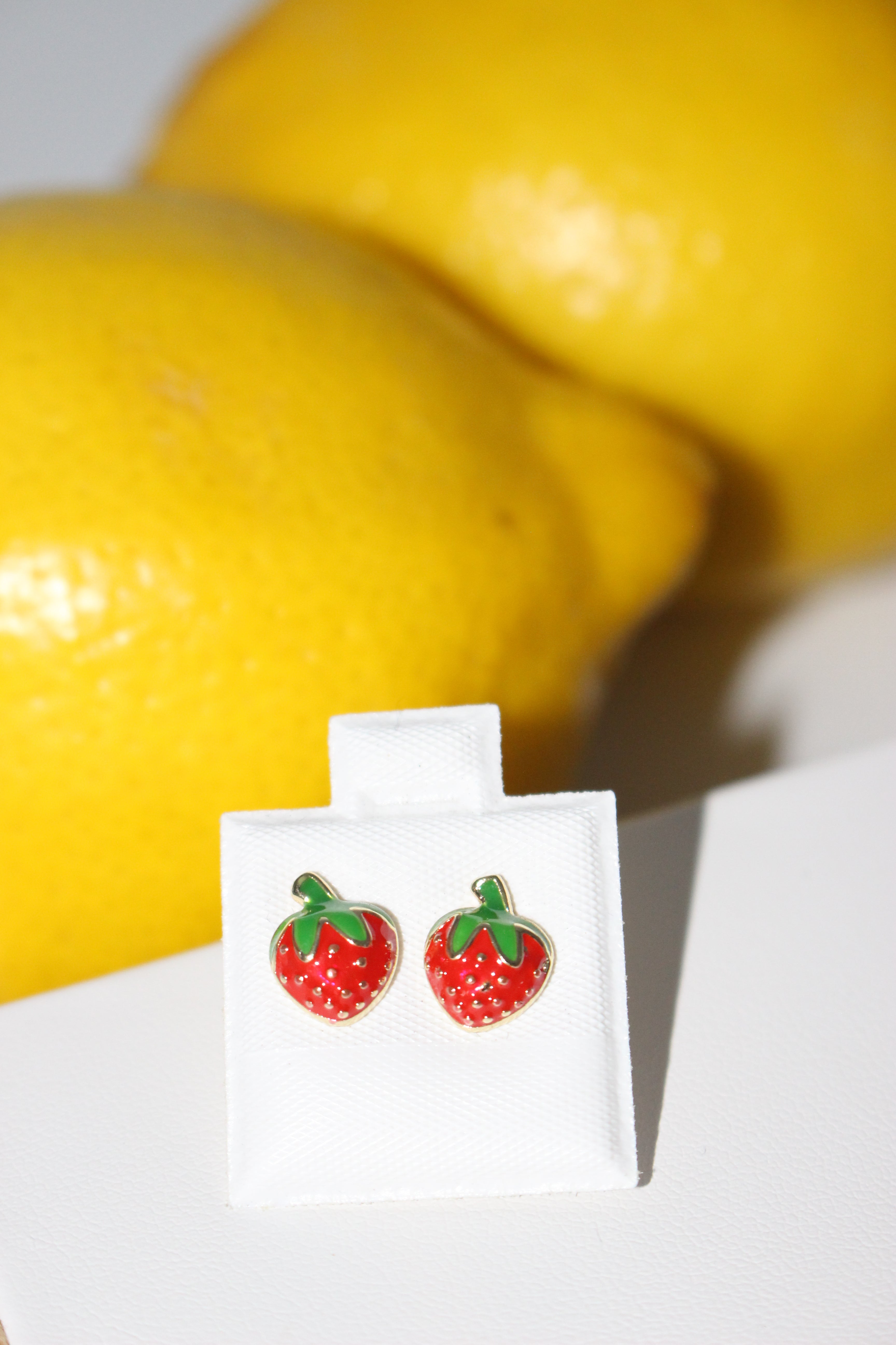 Pair of strawberry-shaped earrings on a white card with lemons in the background