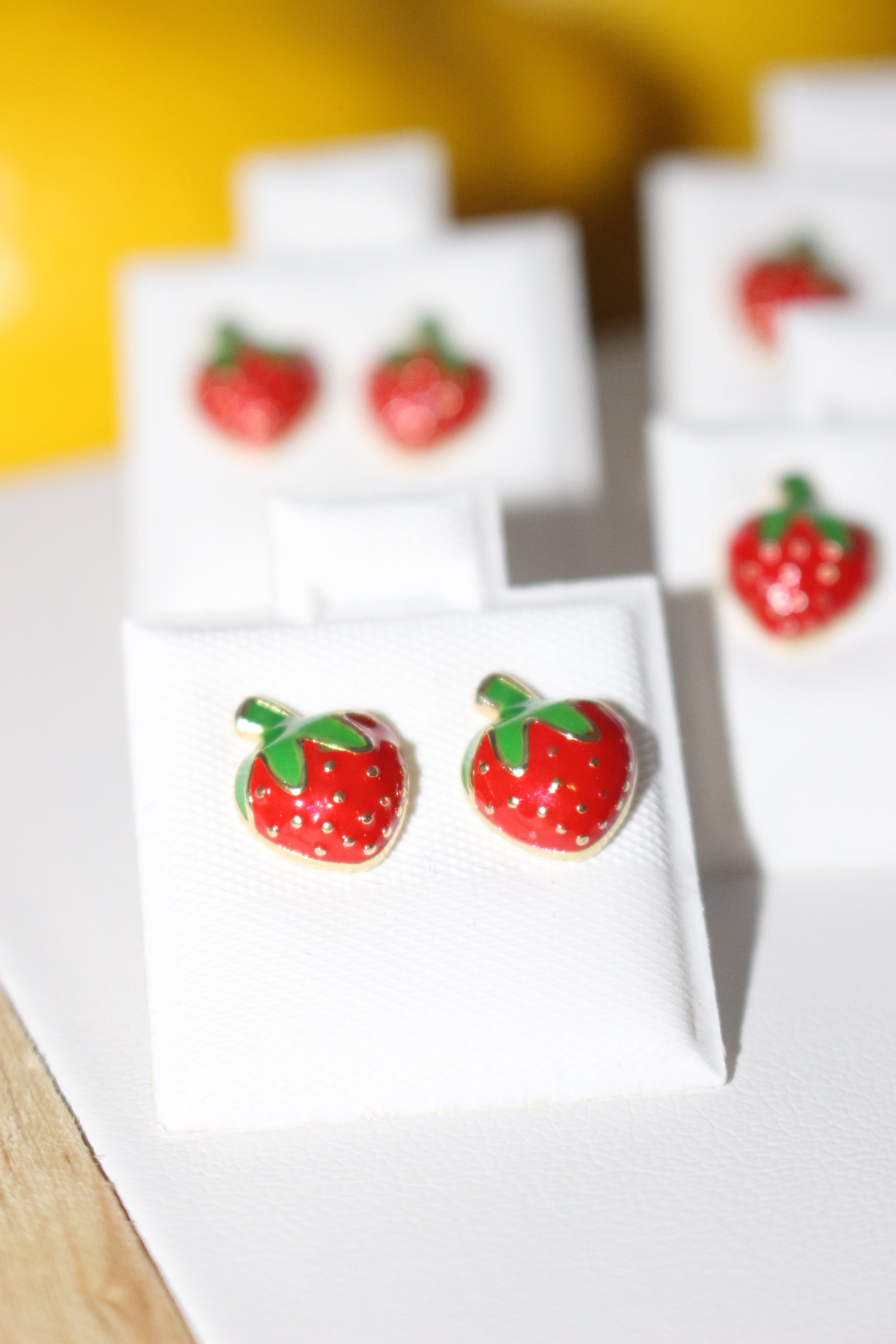 Strawberry-shaped earrings on a white card with a yellow background