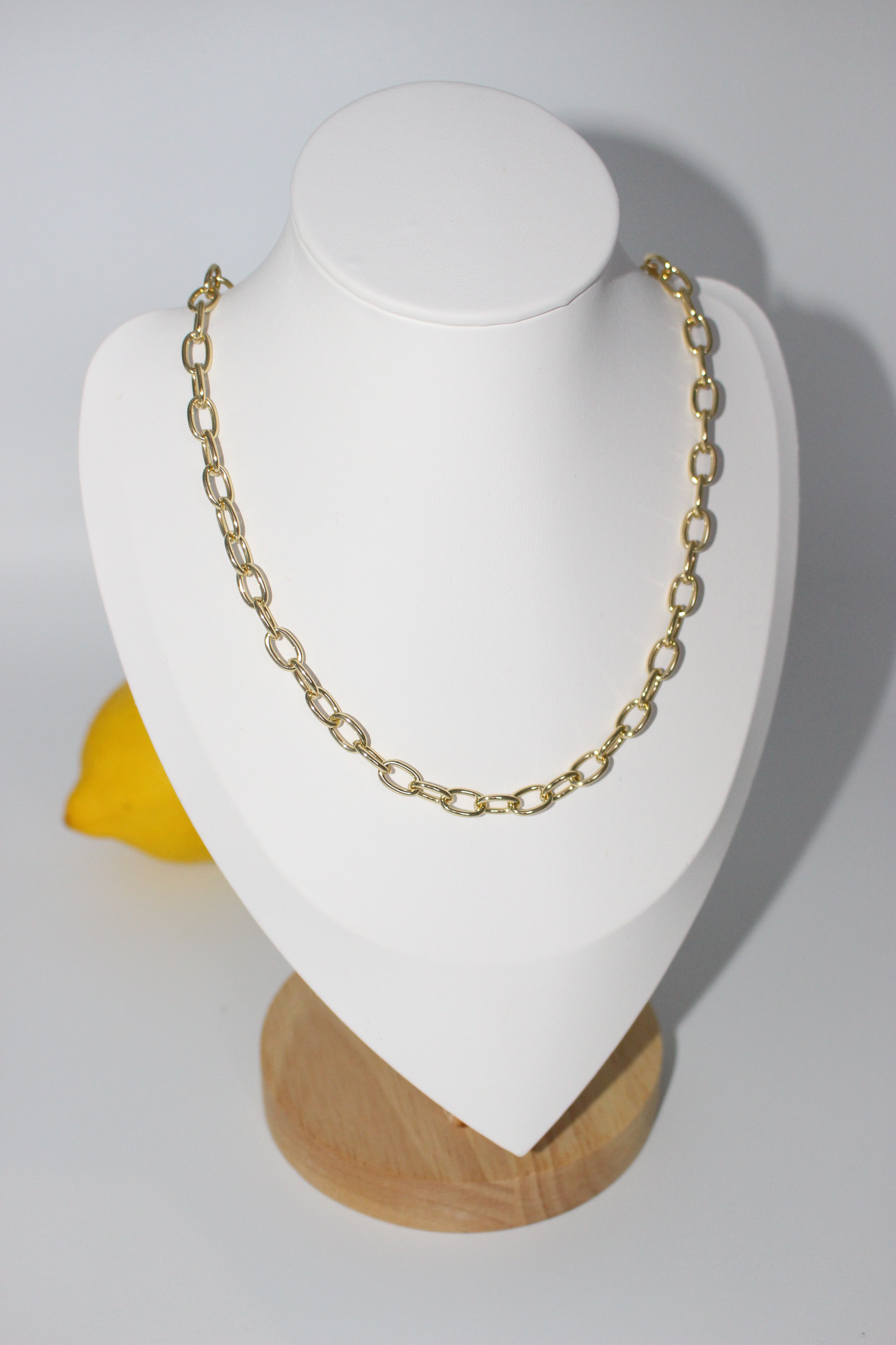 Gold chain necklace on a white jewelry display stand with a yellow object in the background.