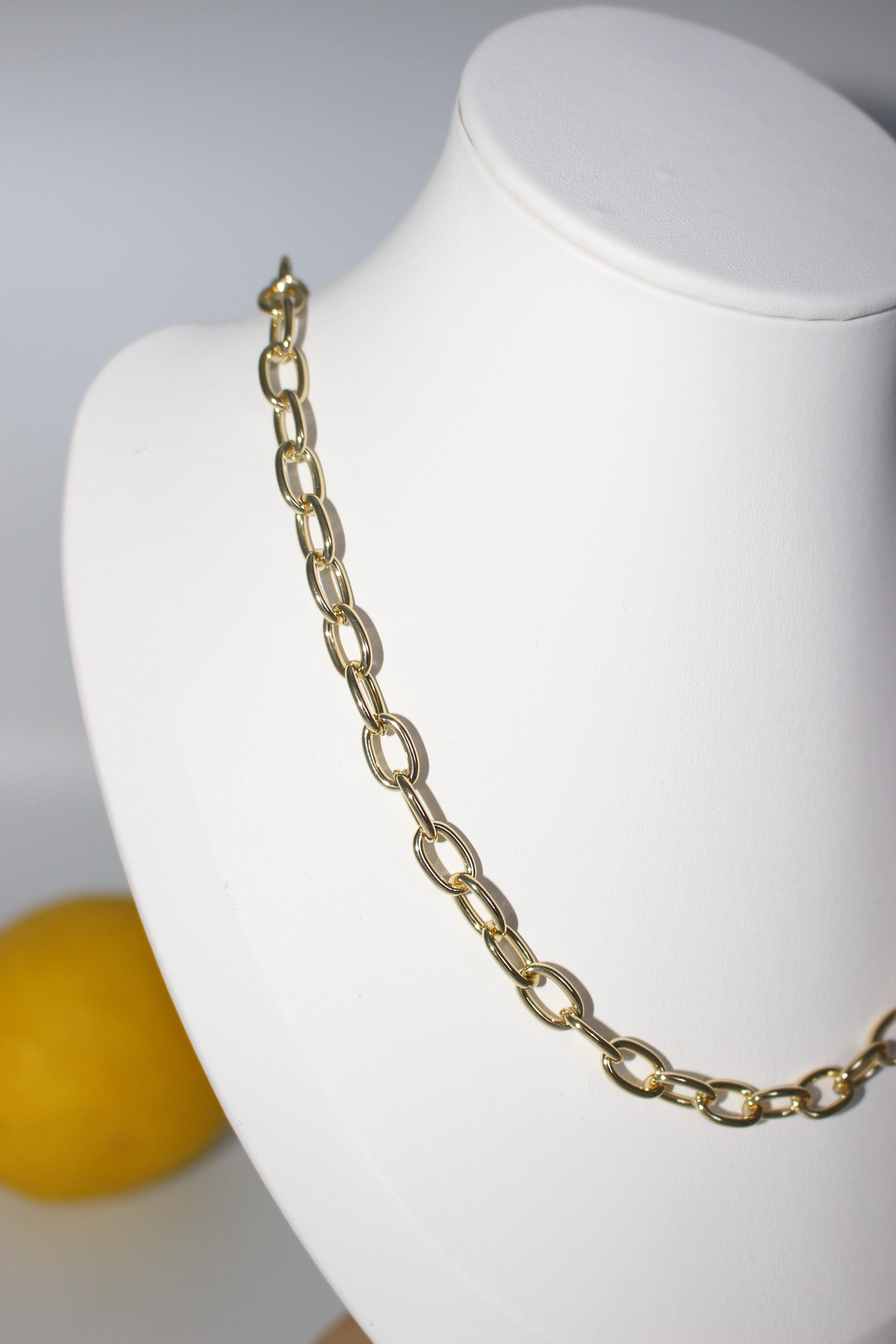 Gold chain bracelet on a white mannequin bust with a yellow object in the background