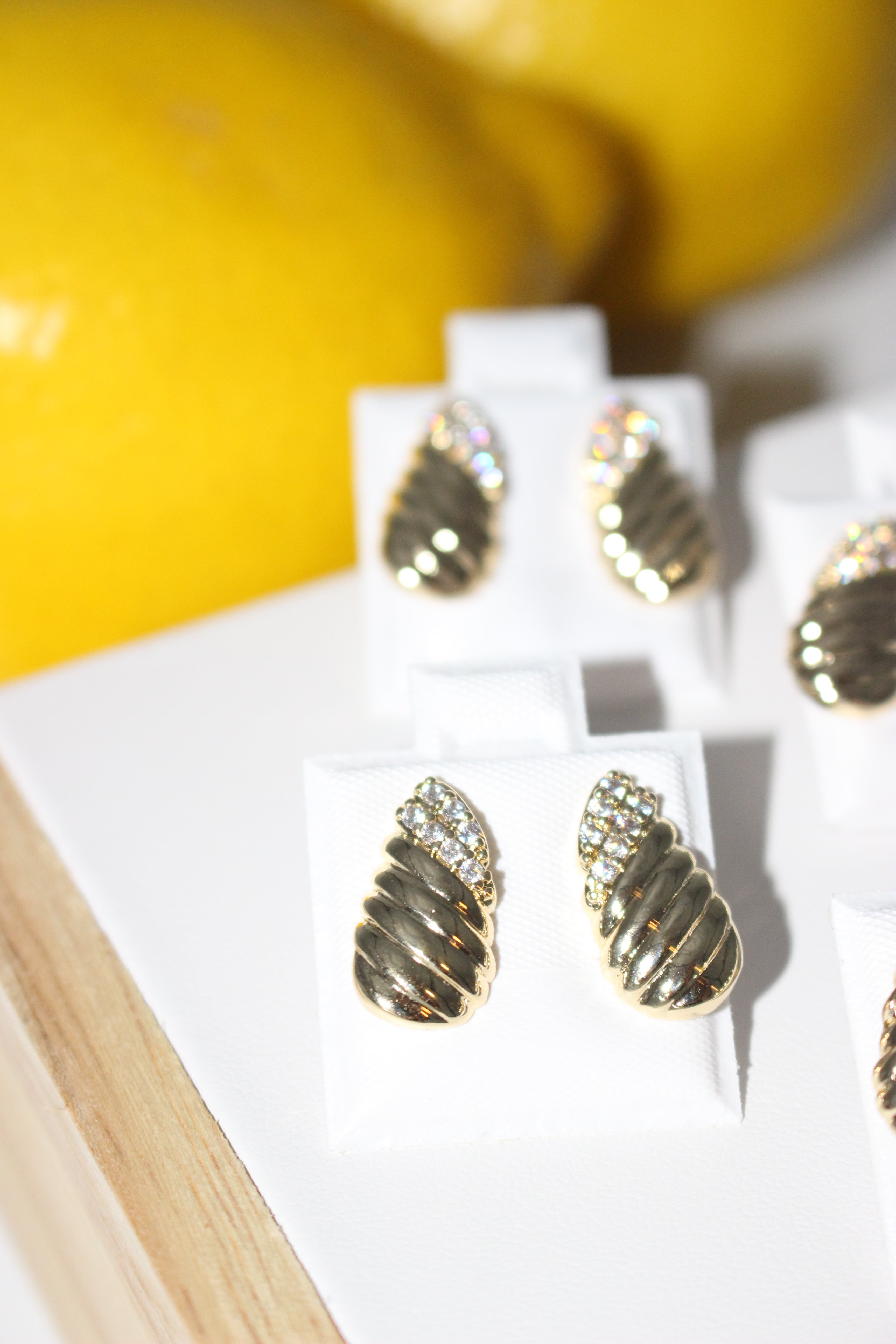 Gold leaf-shaped earrings on a white display stand with a blurred yellow background